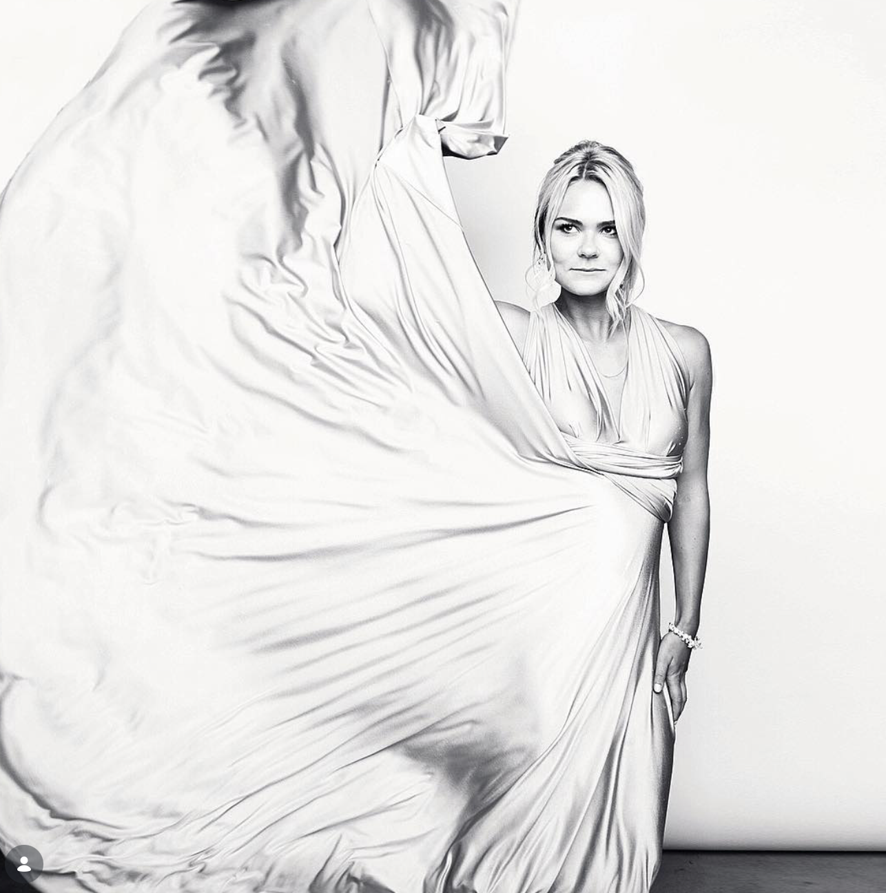 Black and white portrait of a blonde woman in a flowing satin gown, with the voluminous fabric swirling dramatically beside her.
