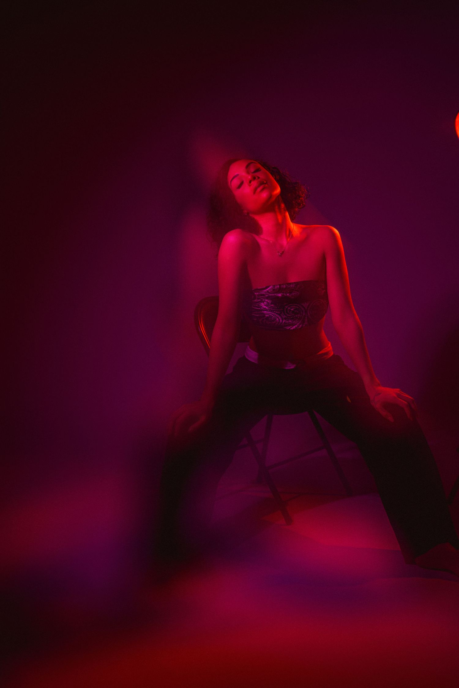 A figure in red lighting performs an artistic dance pose against a dark purple background.