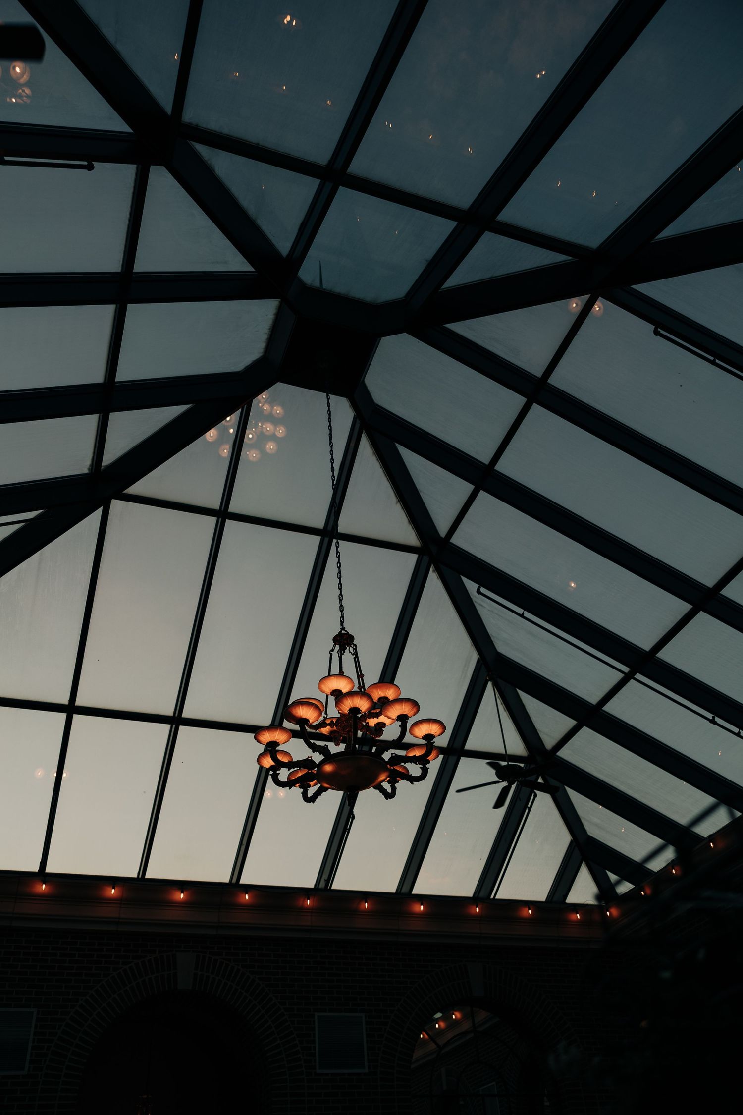 A sequence of photos showing a chandelier silhouetted against a glass ceiling at sunset with dark geometric beams.