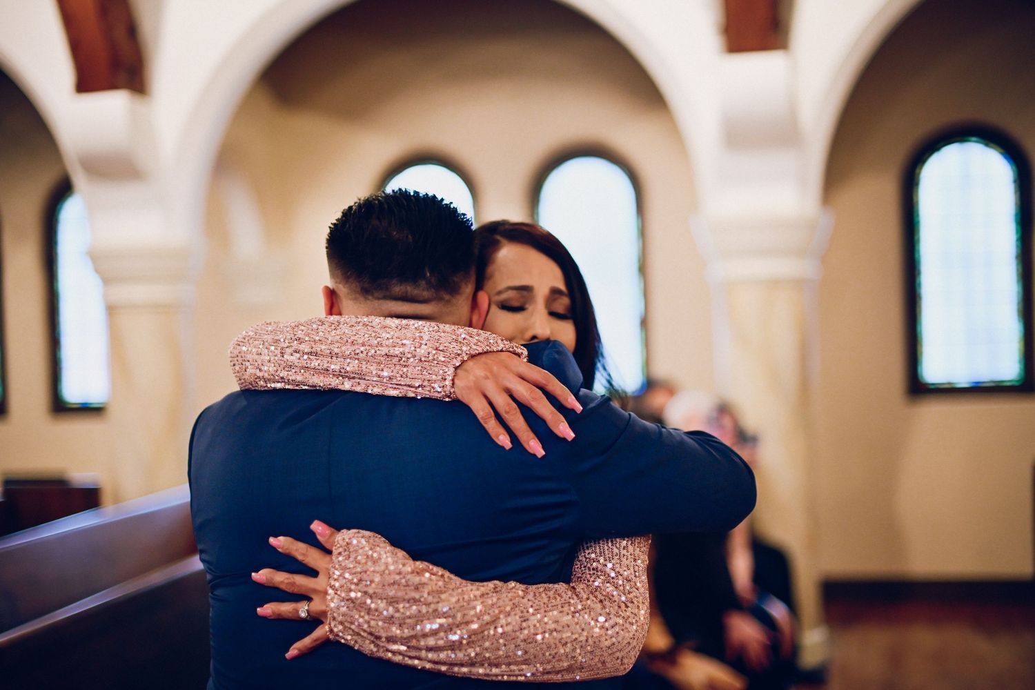 Two people share an emotional embrace during a wedding ceremony in a church setting.