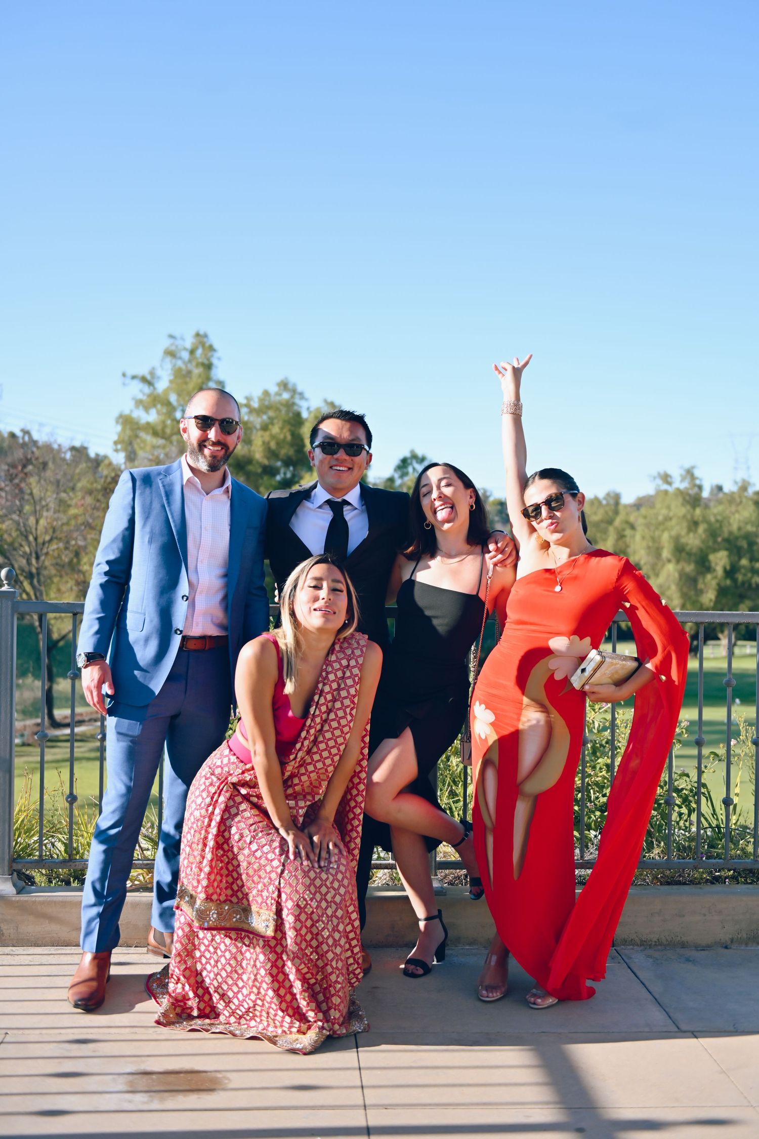 Group of friends posing outdoors in colorful formal attire against a blue sky.