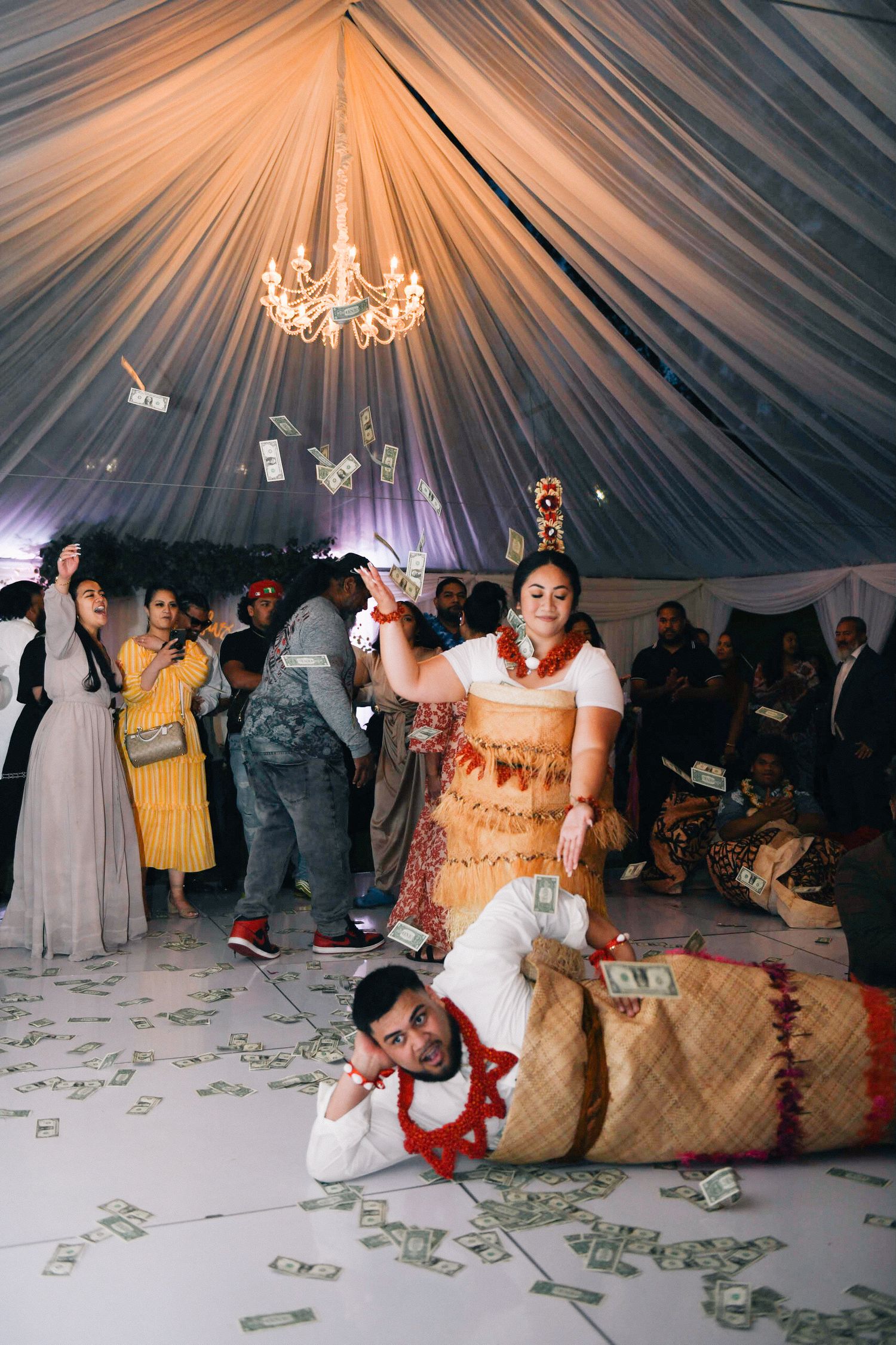 Festive wedding reception with dancing under draped tent ceiling and chandelier lighting.