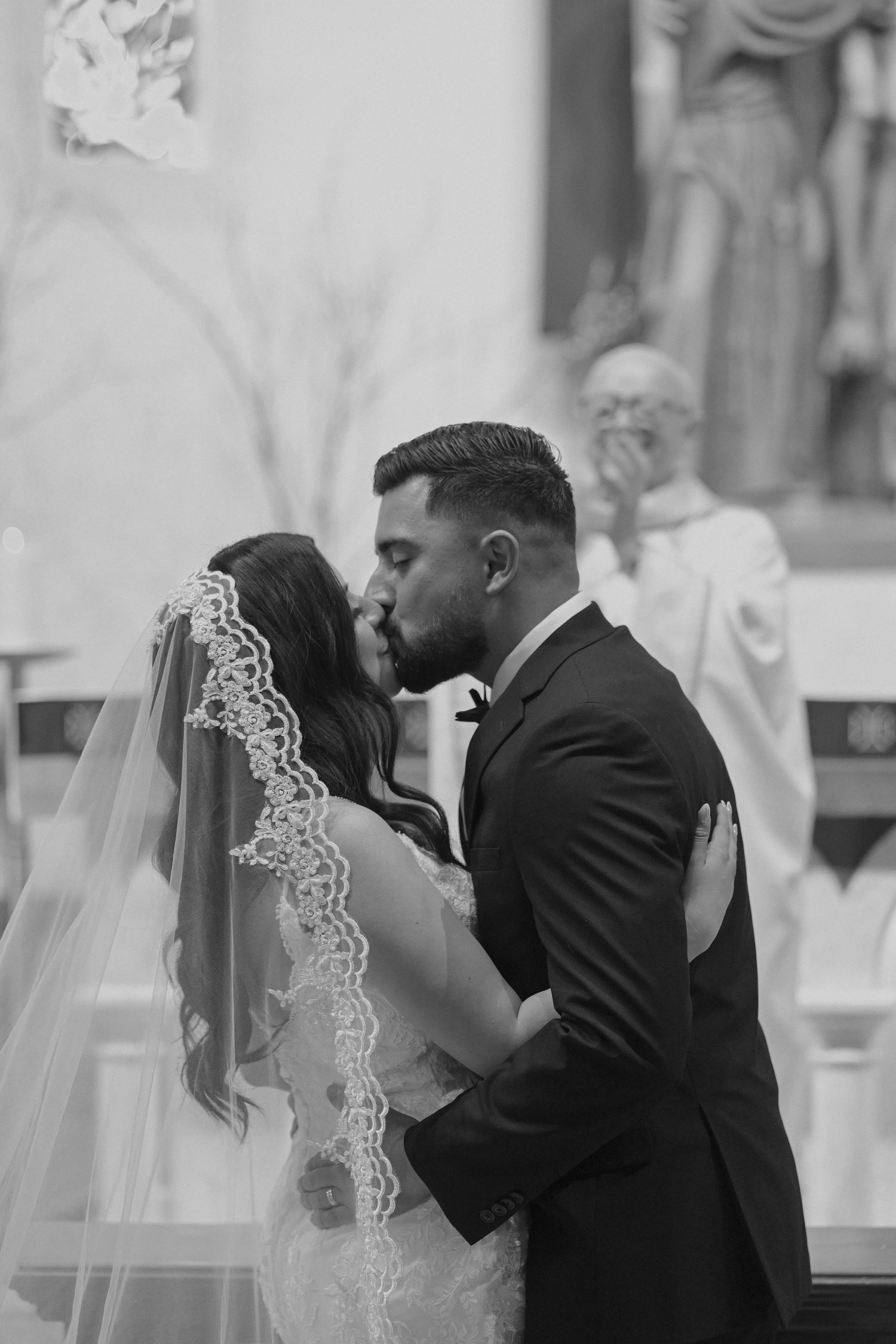Black and white photo of couple kissing during wedding ceremony in church.