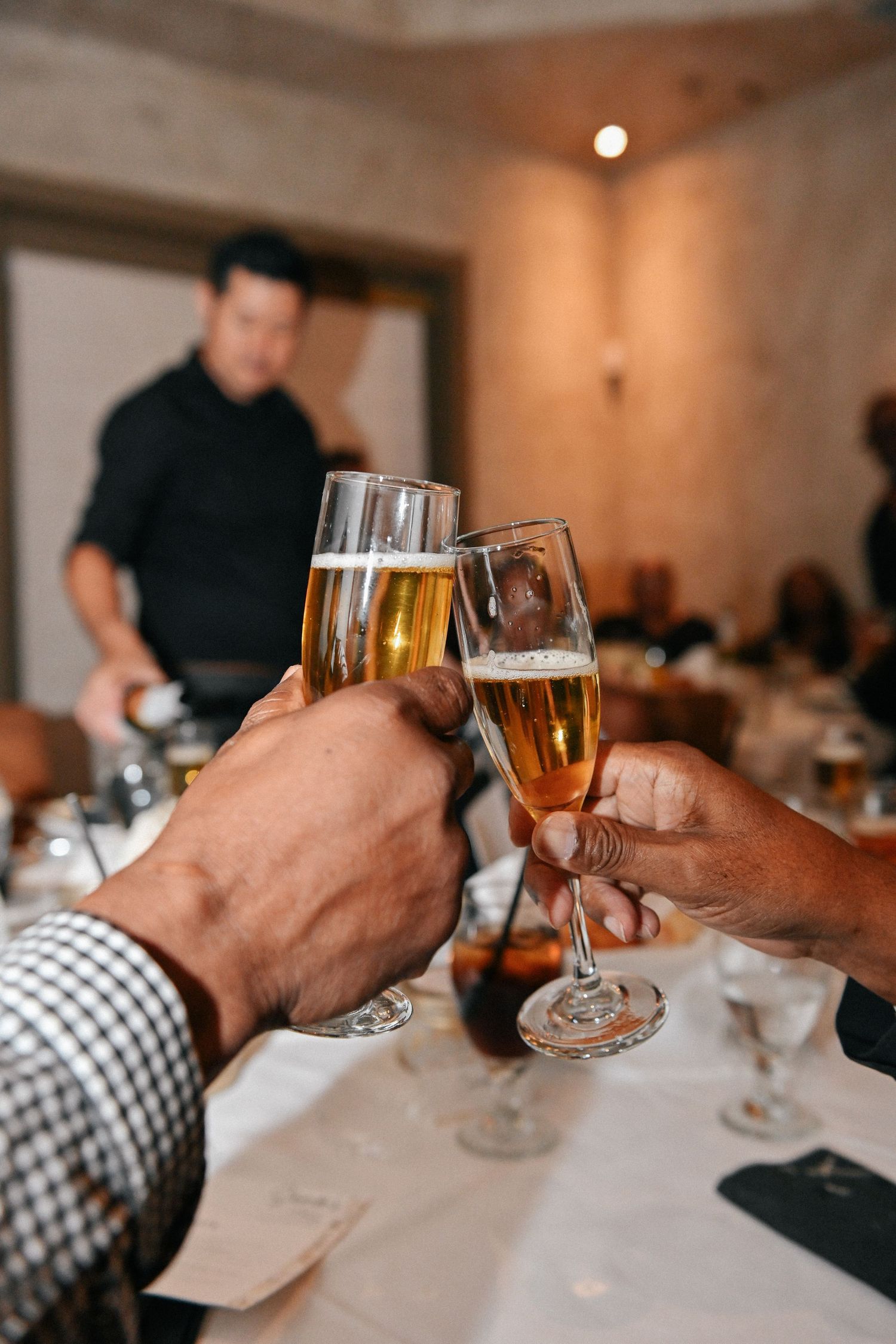 Two hands toasting with champagne flutes at an elegant dinner gathering.