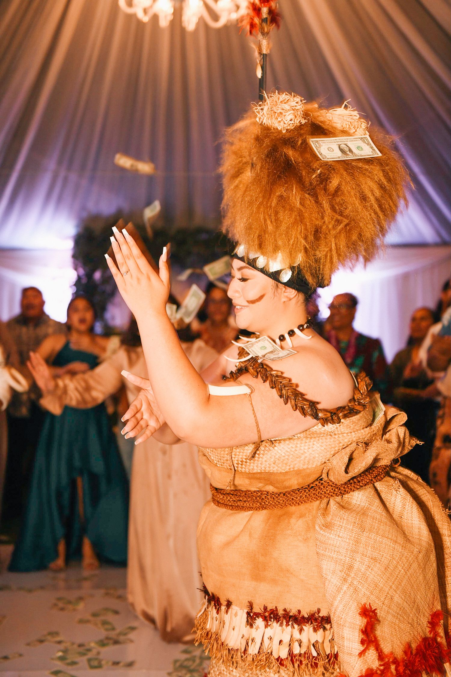 Traditional Polynesian dance performance at wedding reception under draped tent ceiling.