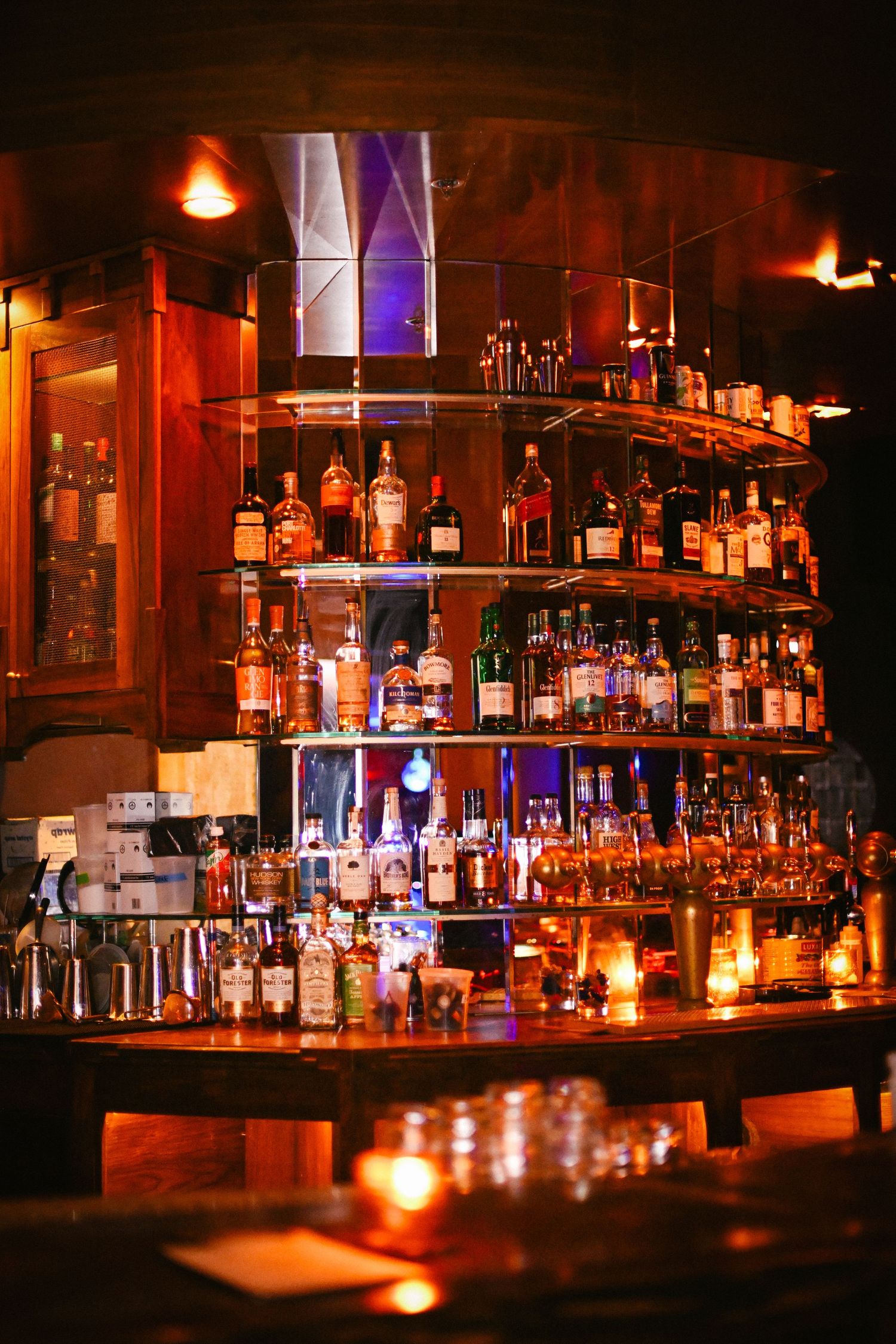 Well-stocked bar shelves illuminated with dramatic red lighting and multiple bottles on display.