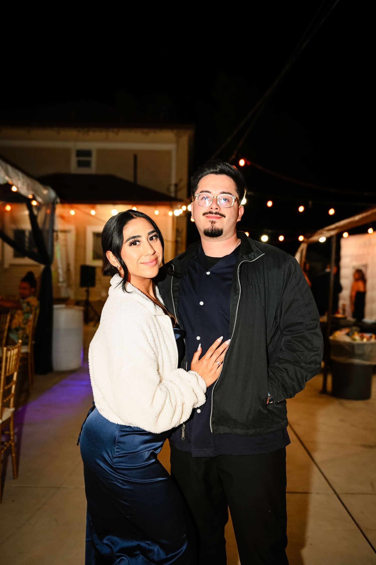 Couple poses together at an outdoor evening event under string lights.