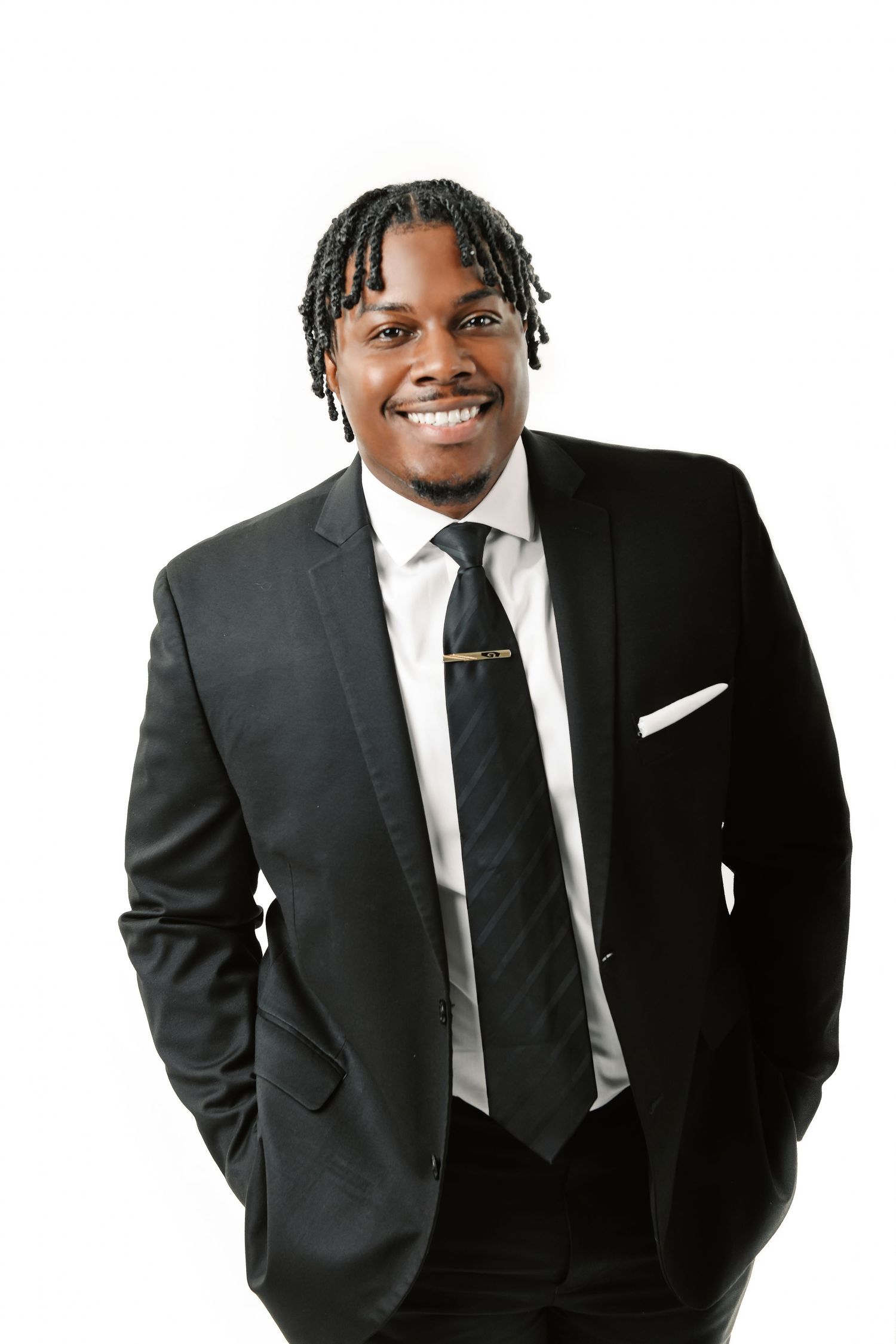 Professional portrait of person in black suit with braided hair against white background.