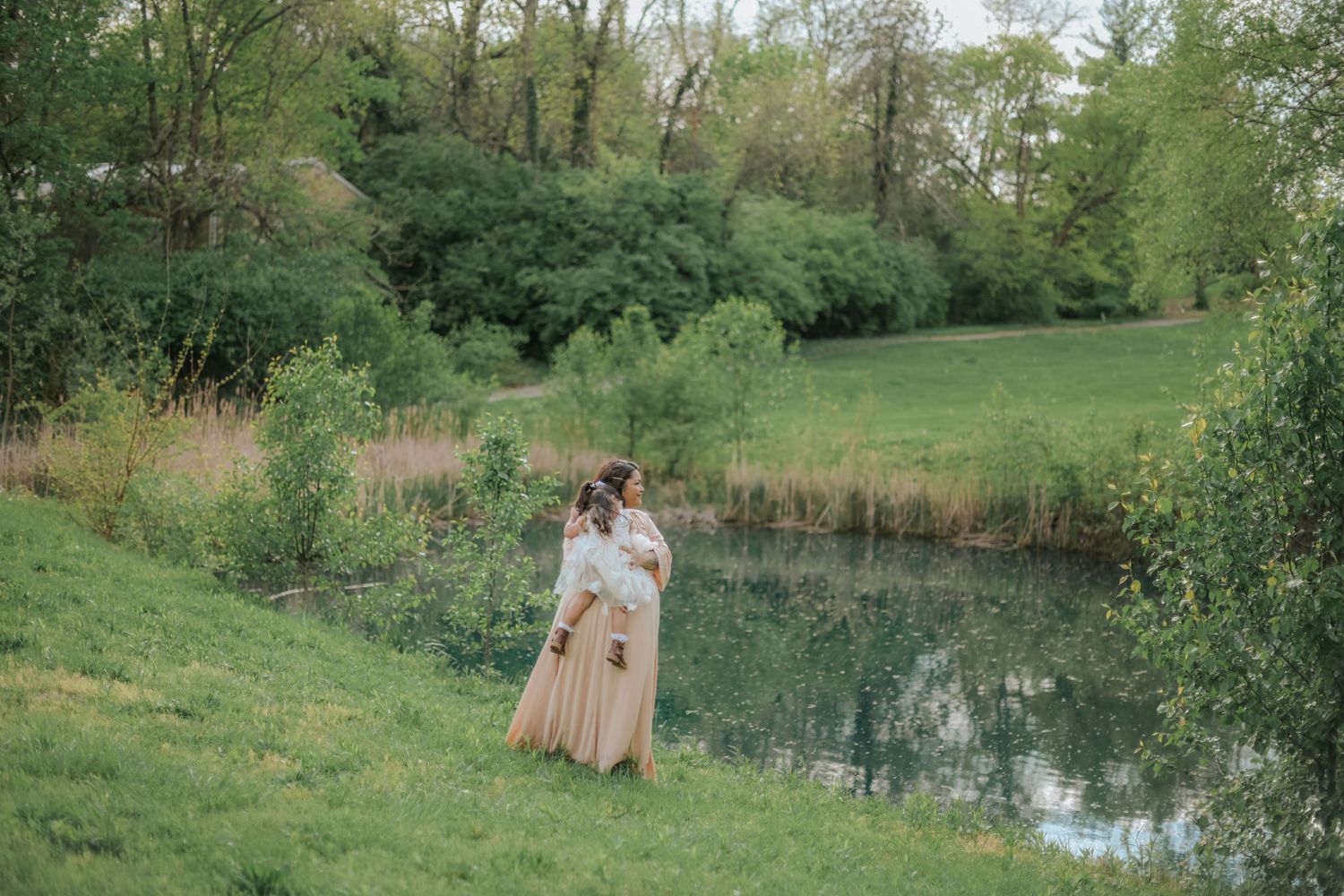 Couple standing by a serene pond surrounded by lush spring greenery.