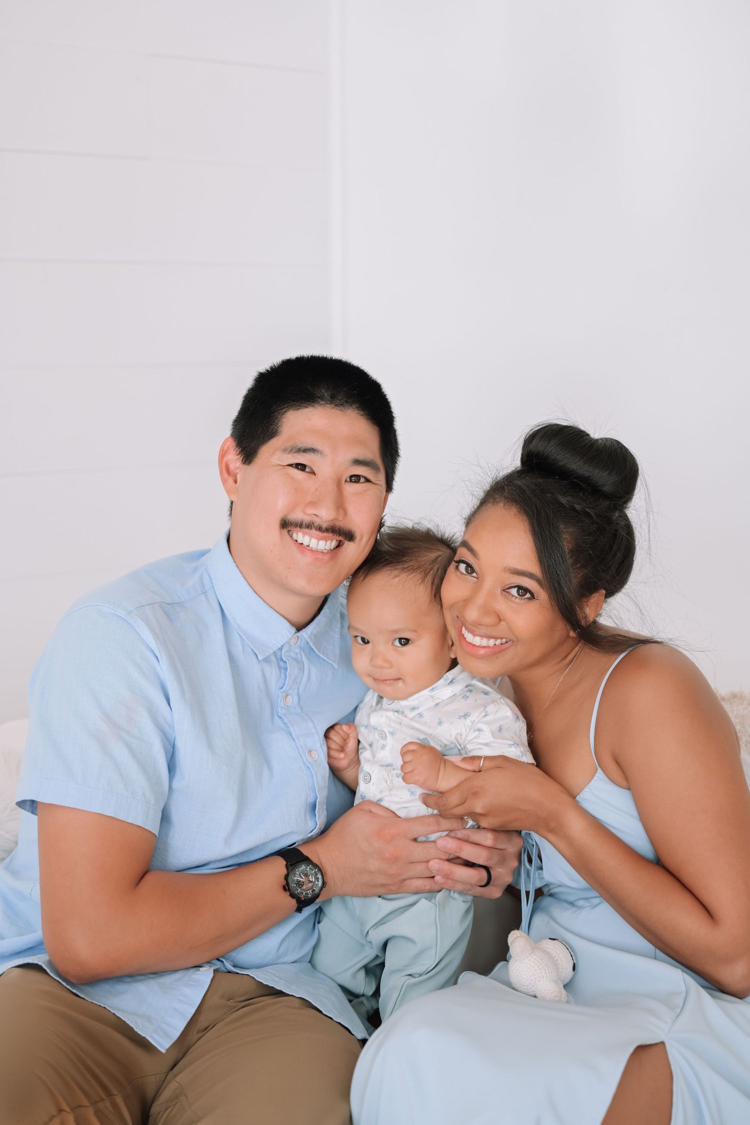 Family of three poses together for studio portrait against white background in coordinating blue outfits.