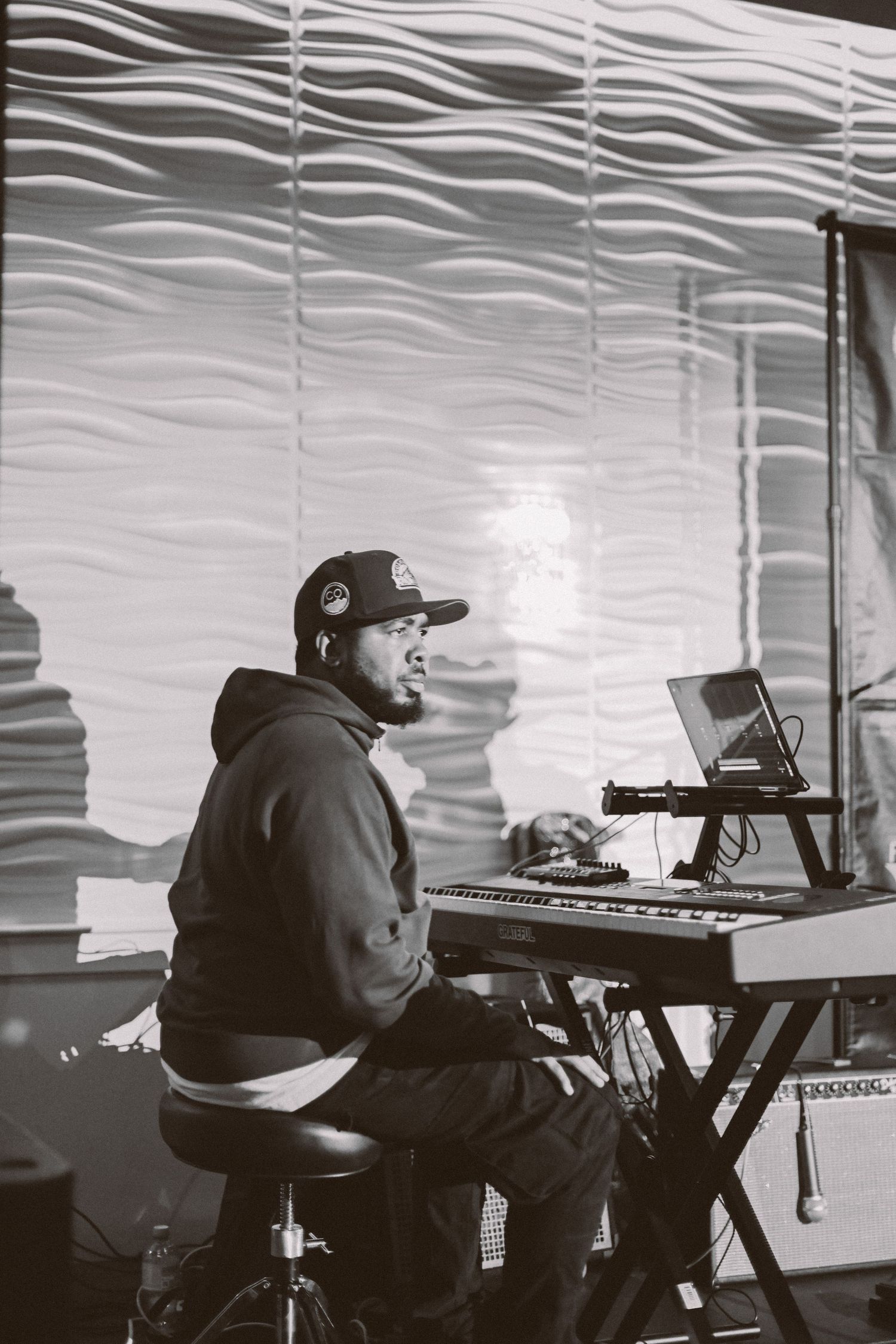 DJ performing at an event with electronic equipment against a textured white wall backdrop.