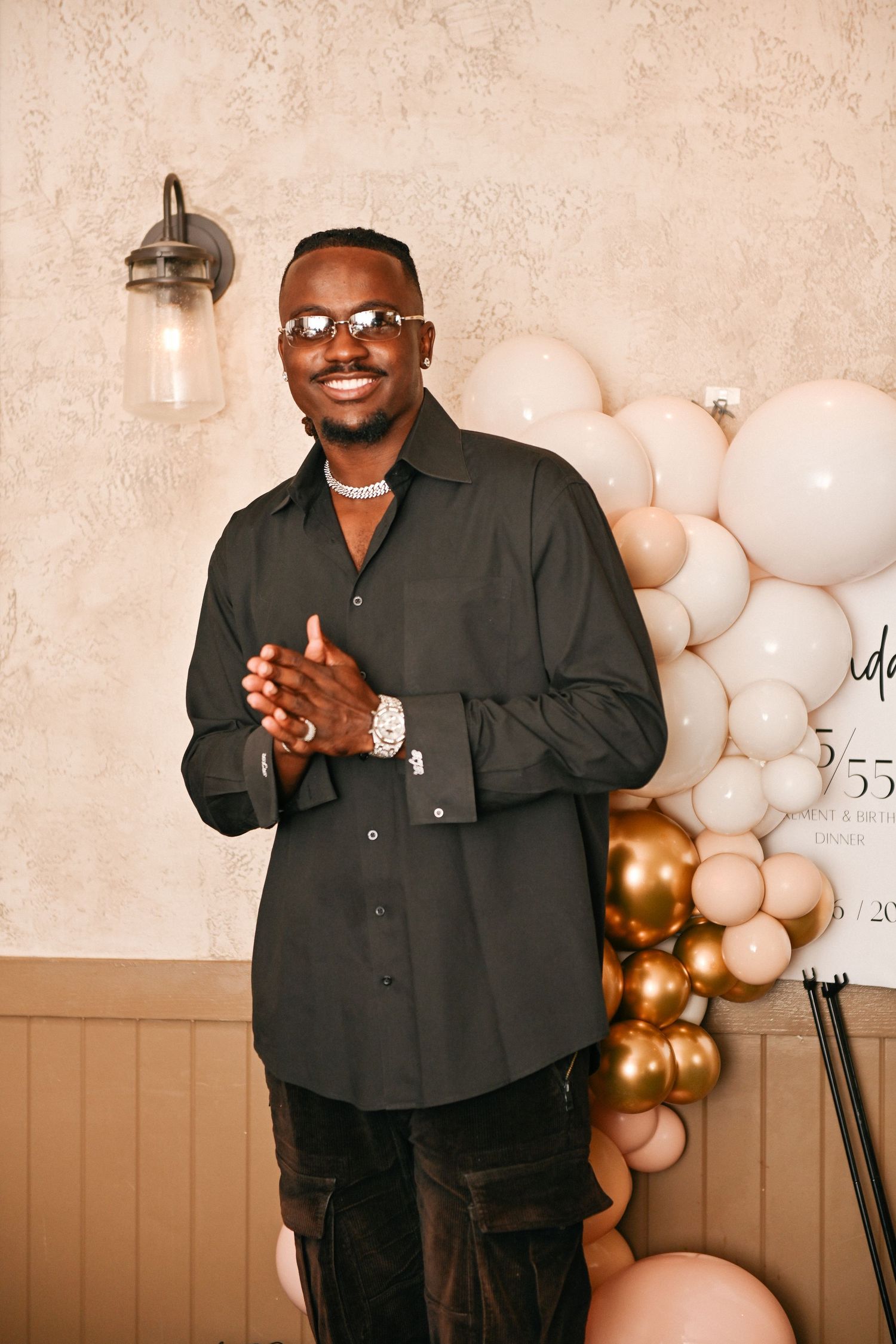 A person poses in front of a decorative balloon arch wall with white and gold balloons.