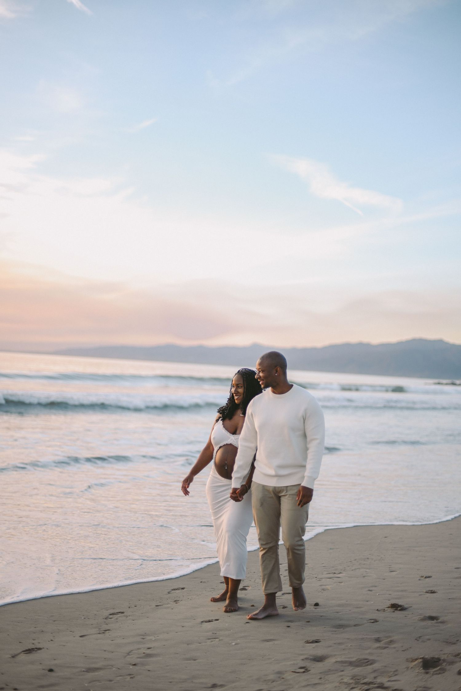 A romantic beach scene with a couple walking together at sunset along the shore.