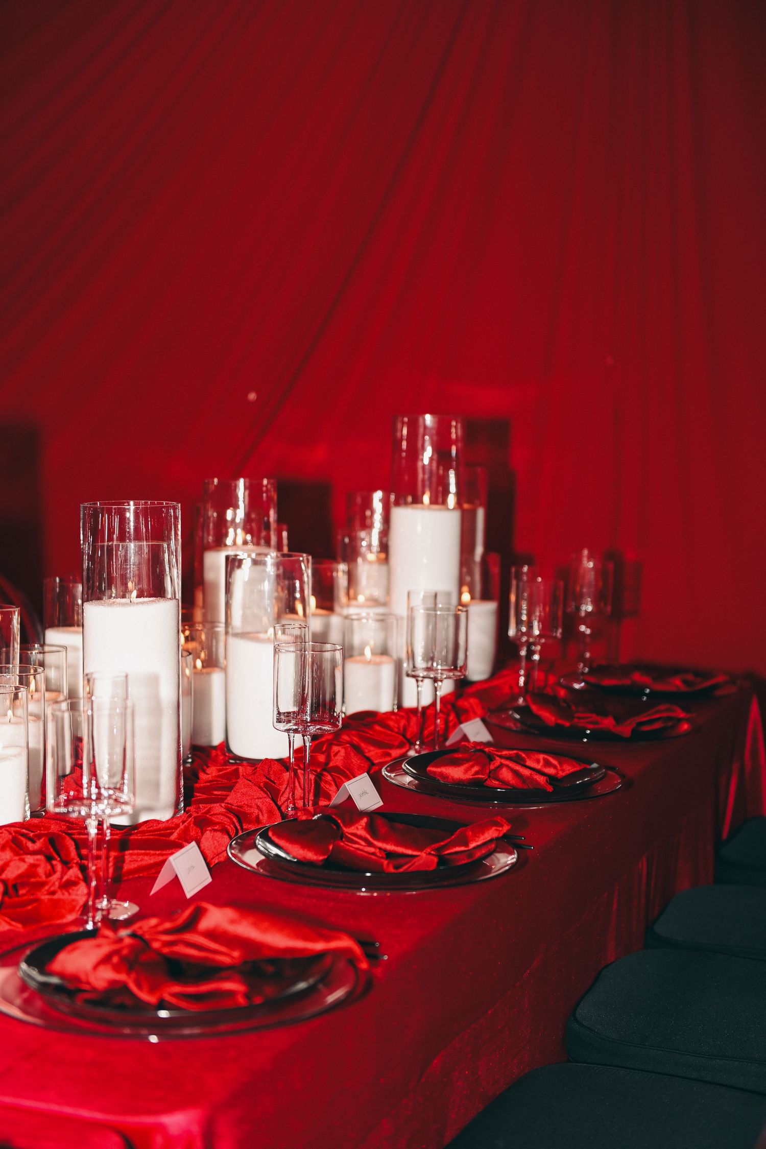 Elegant table setting with red tablecloth, white candles, and place settings in dramatic lighting.