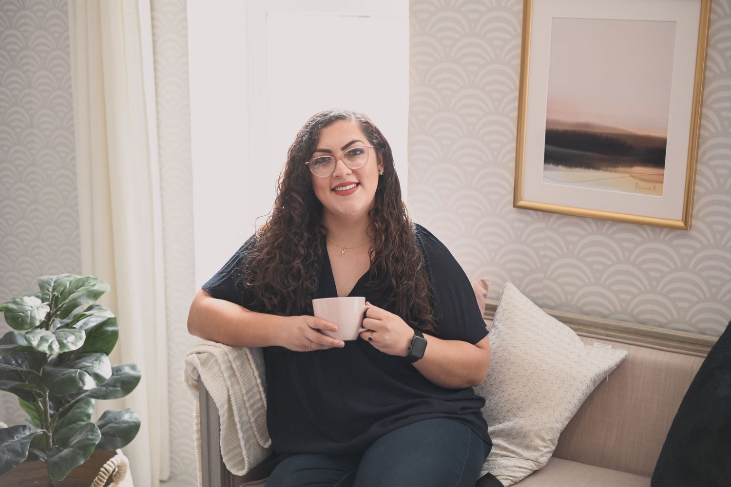 Person smiling while holding coffee cup in bright living room setting.