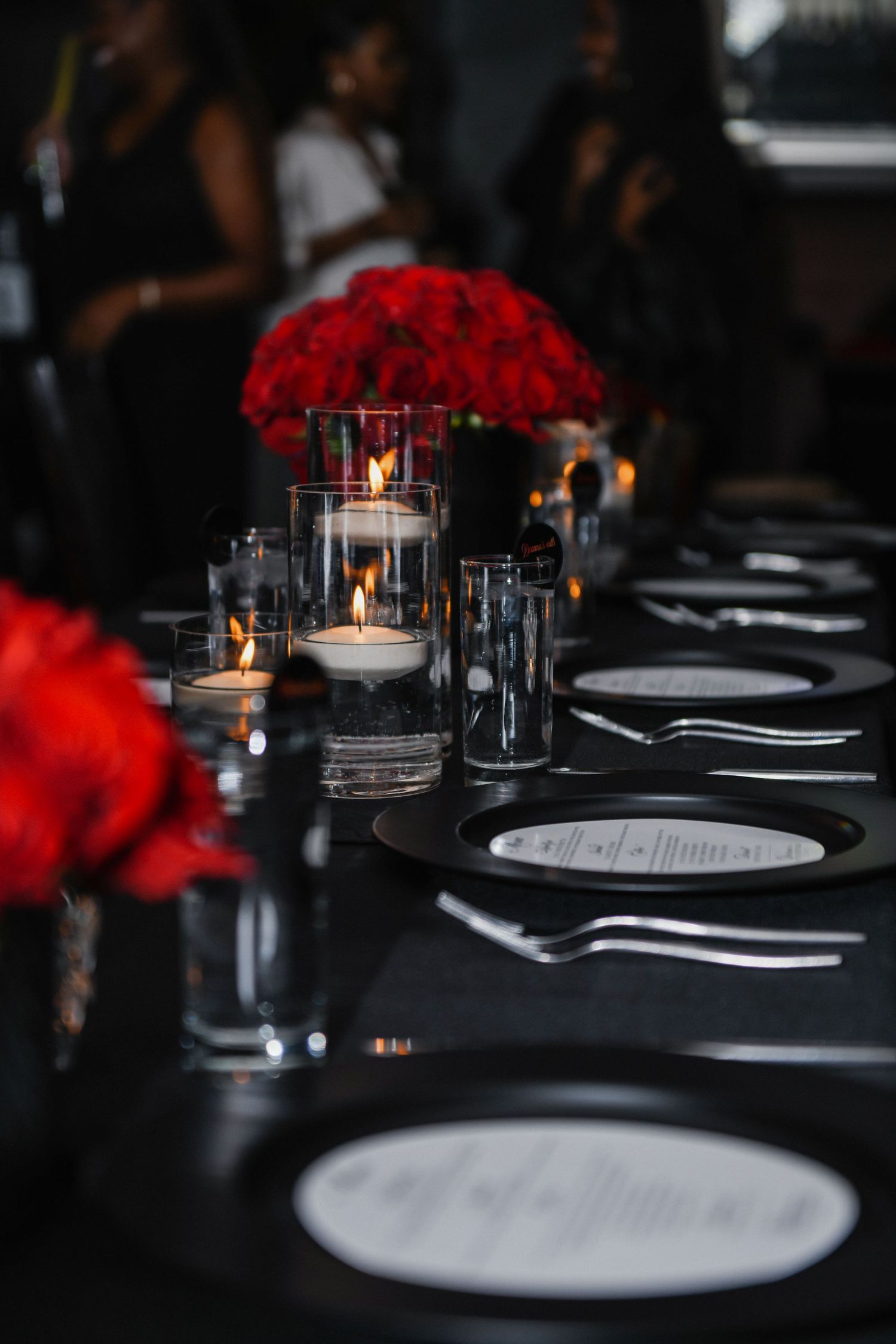 Elegant table setting with red rose centerpieces and candlelight on black tablecloth.