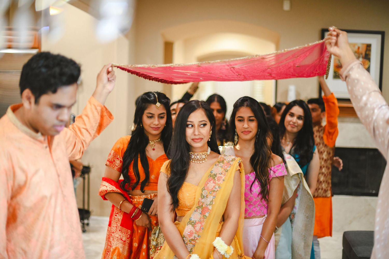 Traditional Indian wedding ceremony with colorful red and orange fabric held above participants.