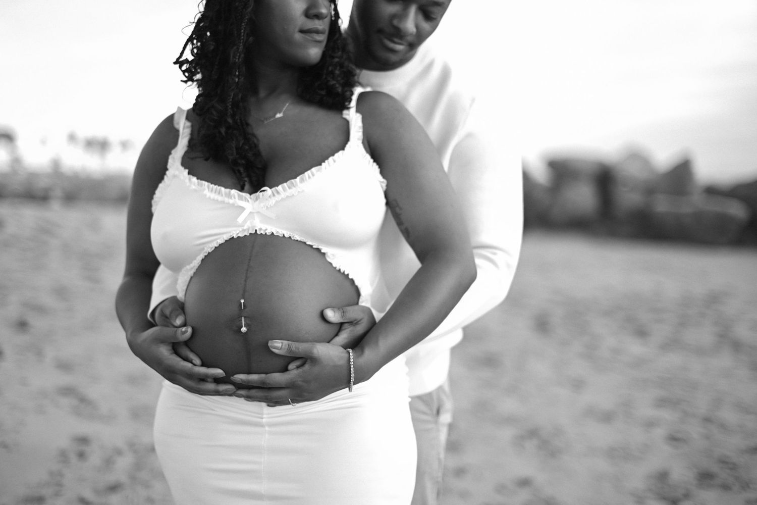 A black and white maternity photo showing a couple embracing on the beach.