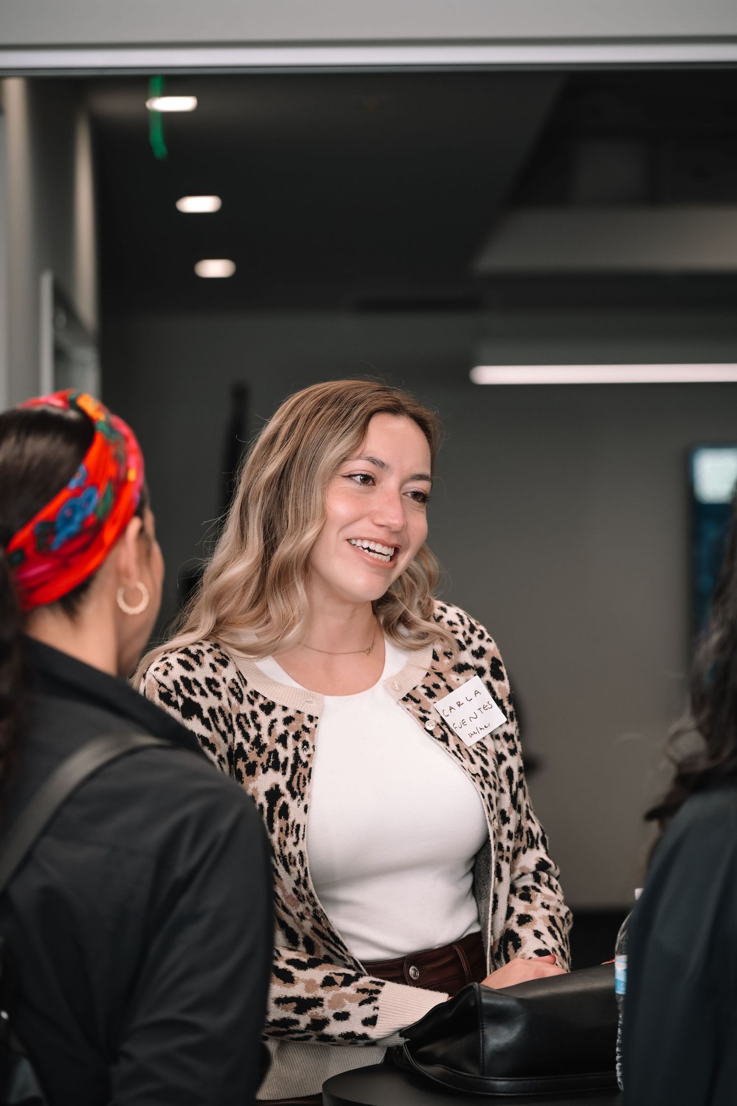 People engage in conversation in an office space with one wearing a trendy leopard print cardigan over a white top.