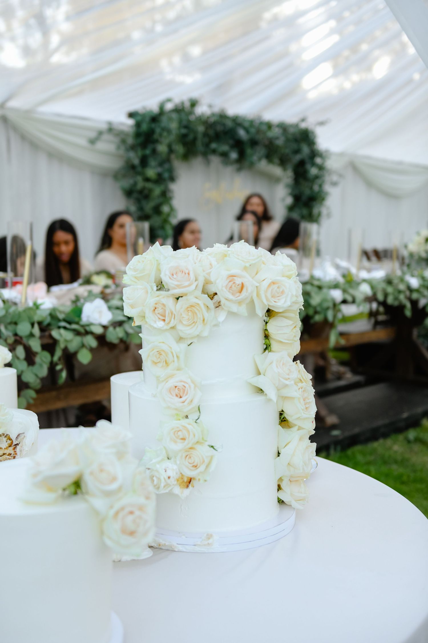 Elegant white wedding cake decorated with cascading white roses on display at reception.