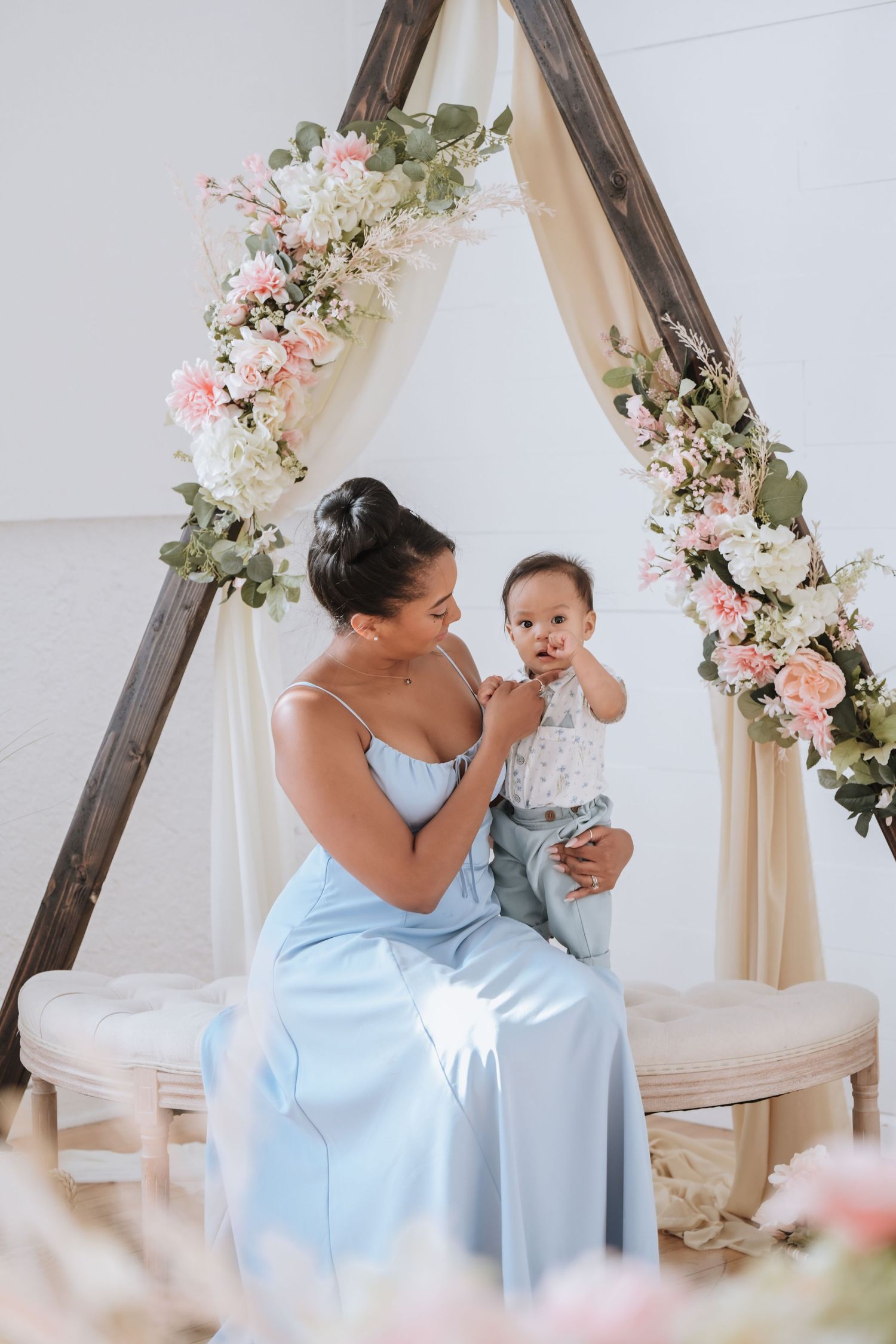 Tender moment between parent and child under a floral arch decorated with white and pink blooms.
