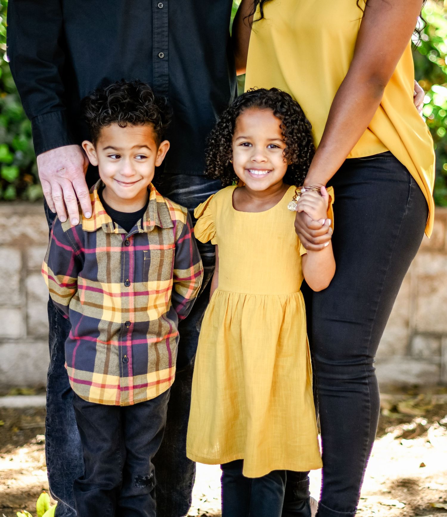 Cropped view of children holding hands with parents in coordinated yellow and plaid outfits.