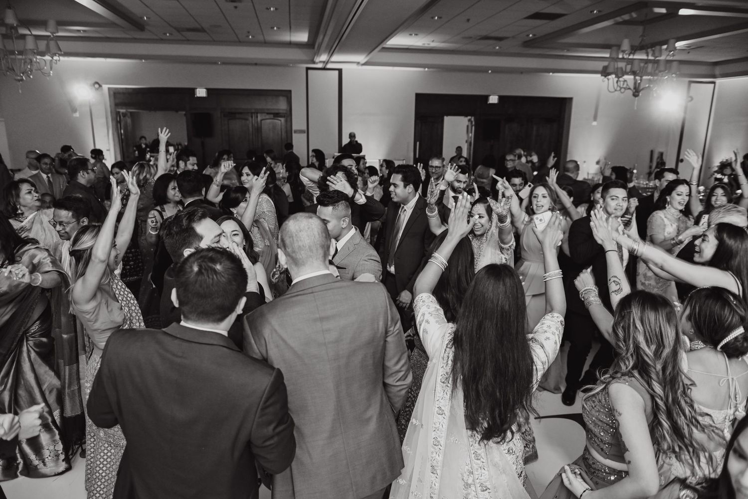 Black and white photo of crowded wedding reception dance floor with guests celebrating.