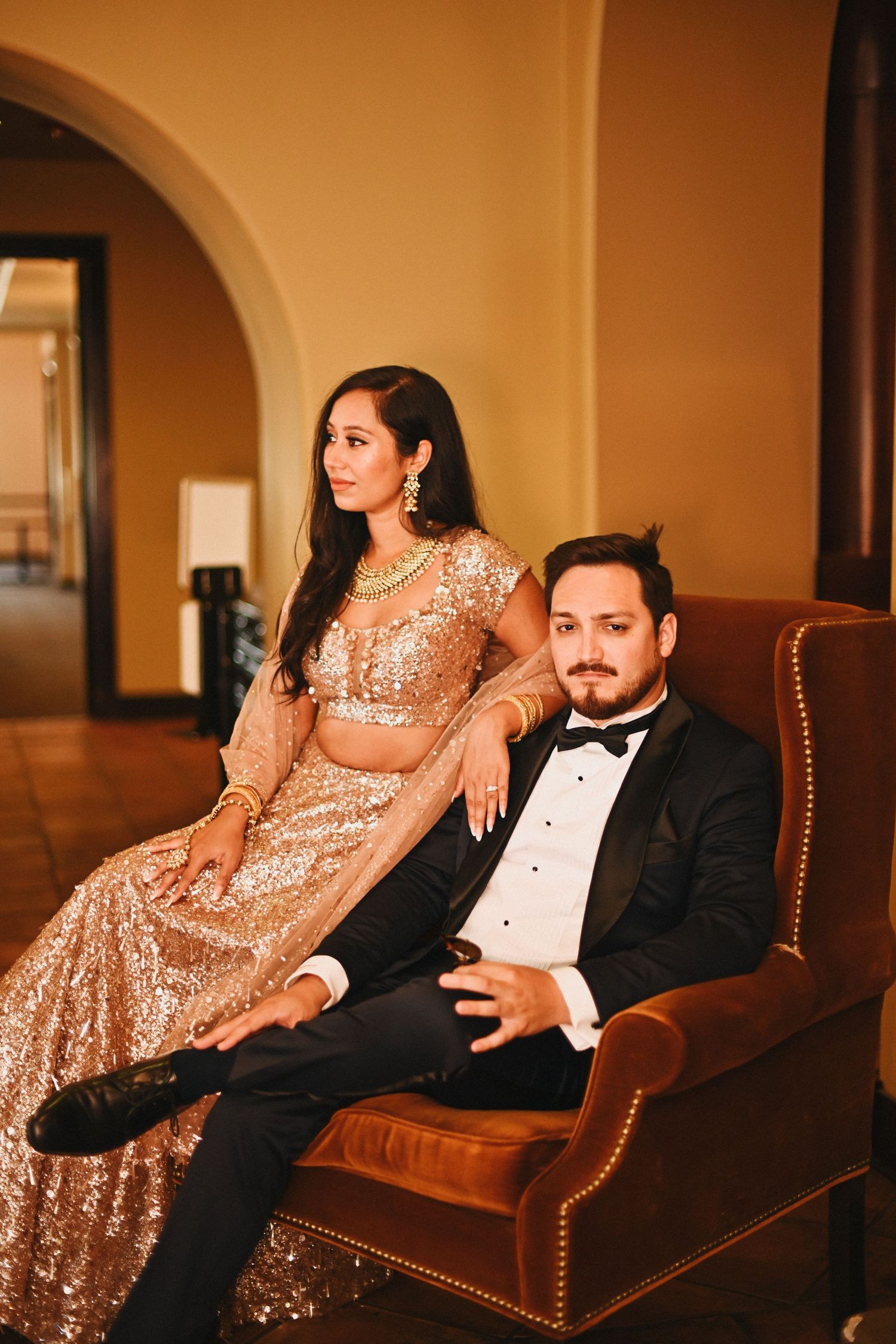Formal couple relaxing in leather armchair in elegant indoor setting.
