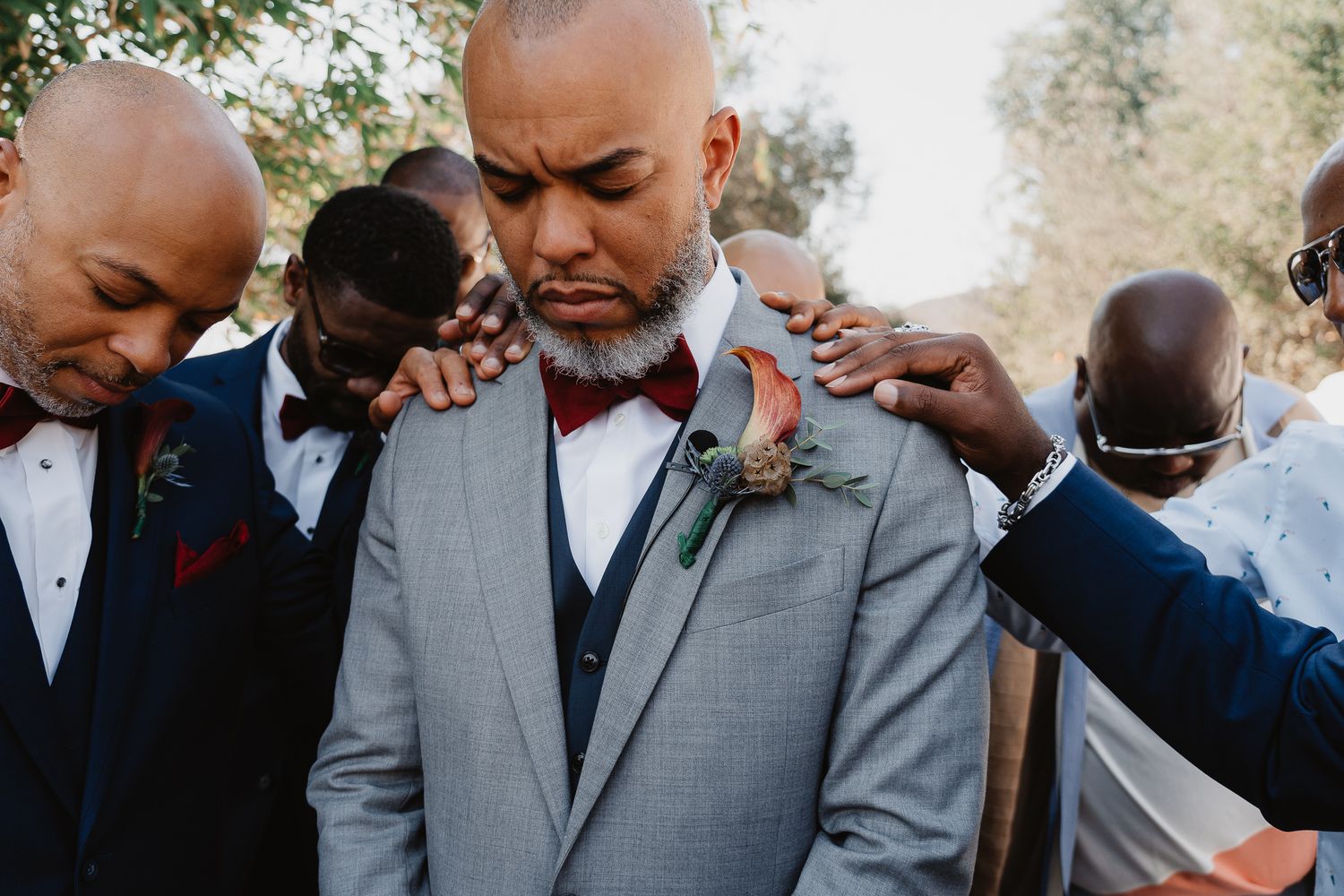 Emotional moment during outdoor wedding ceremony with formal attire and red boutonnieres.