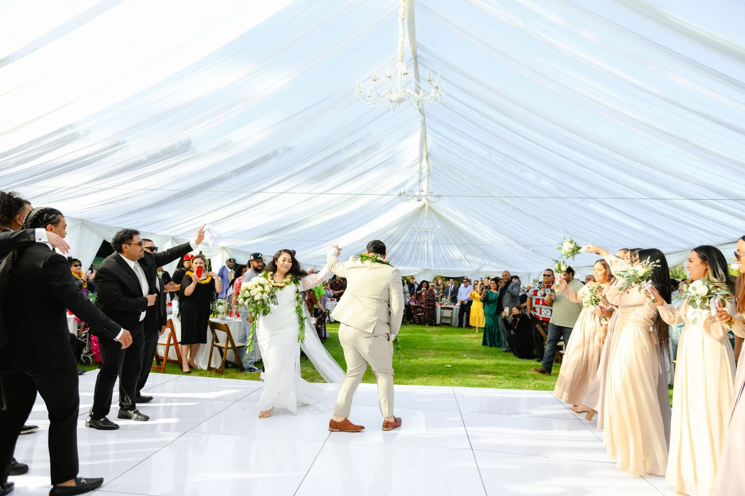 Elegant wedding celebration under a white tent with guests lined up on both sides of a dance floor.