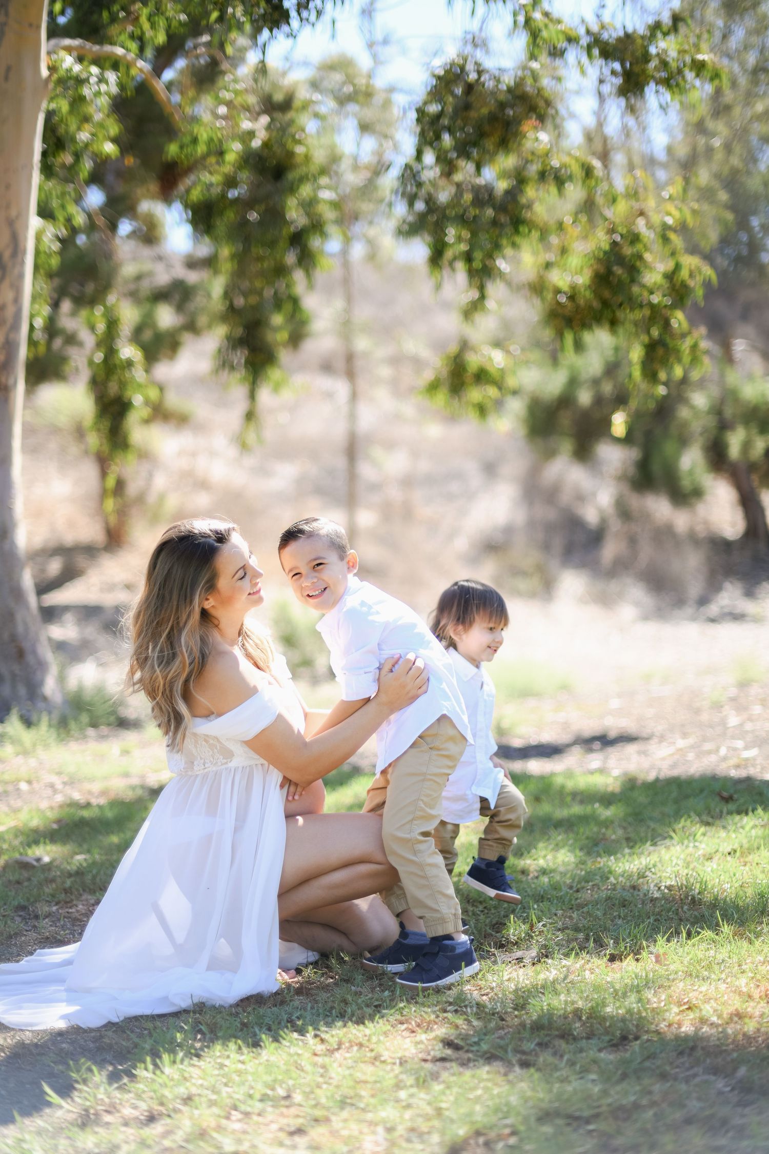 Family in white outfits playing together under a large tree in a sunny park.