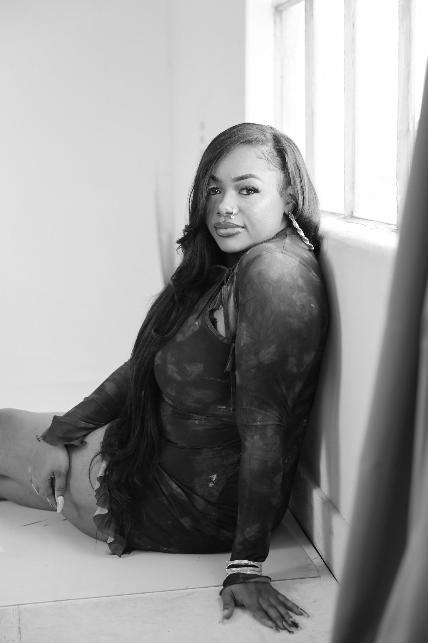 Black and white portrait of woman in dark top sitting by bright windows.
