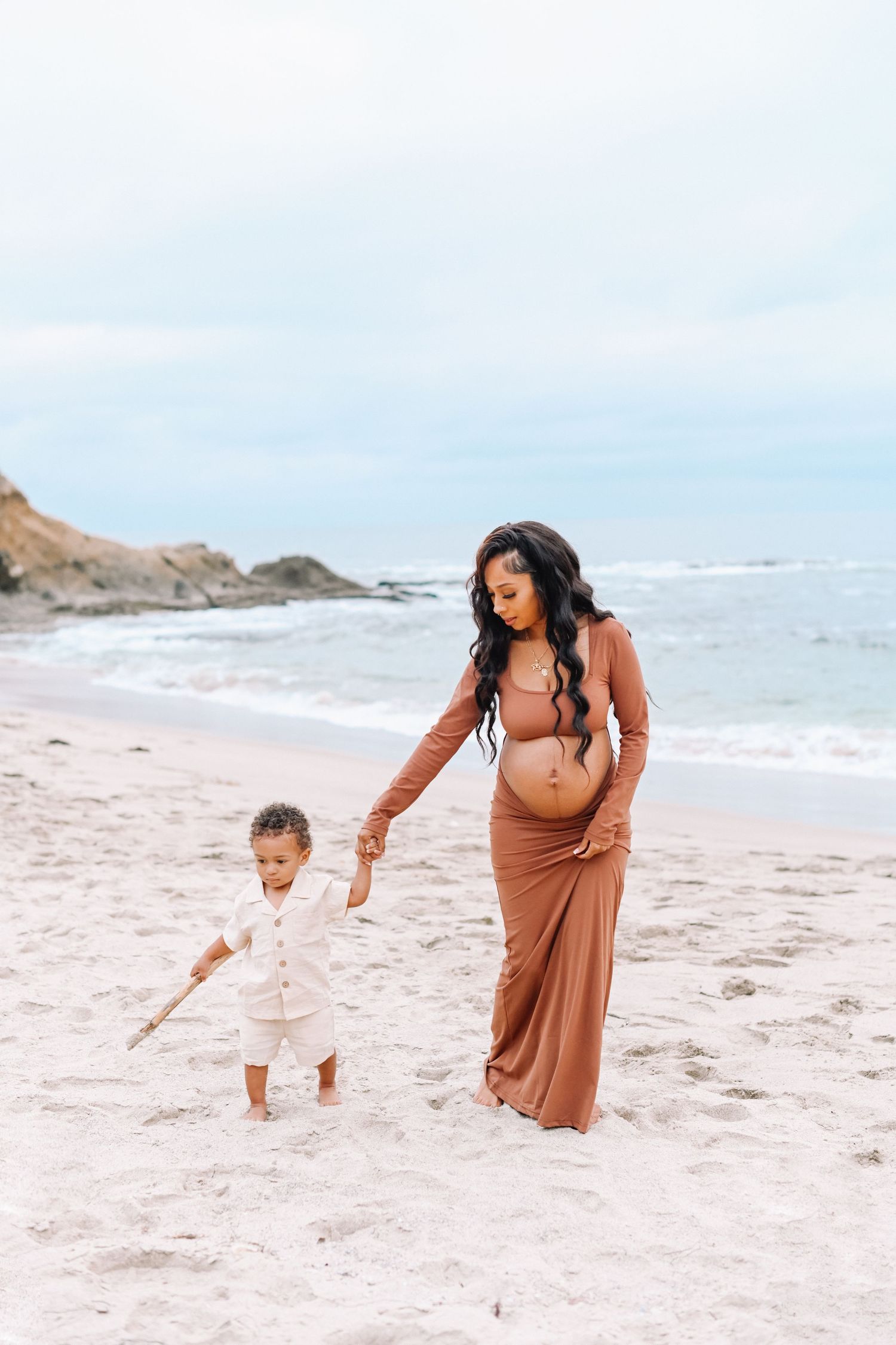 Mother and child walking hand in hand on sandy beach.