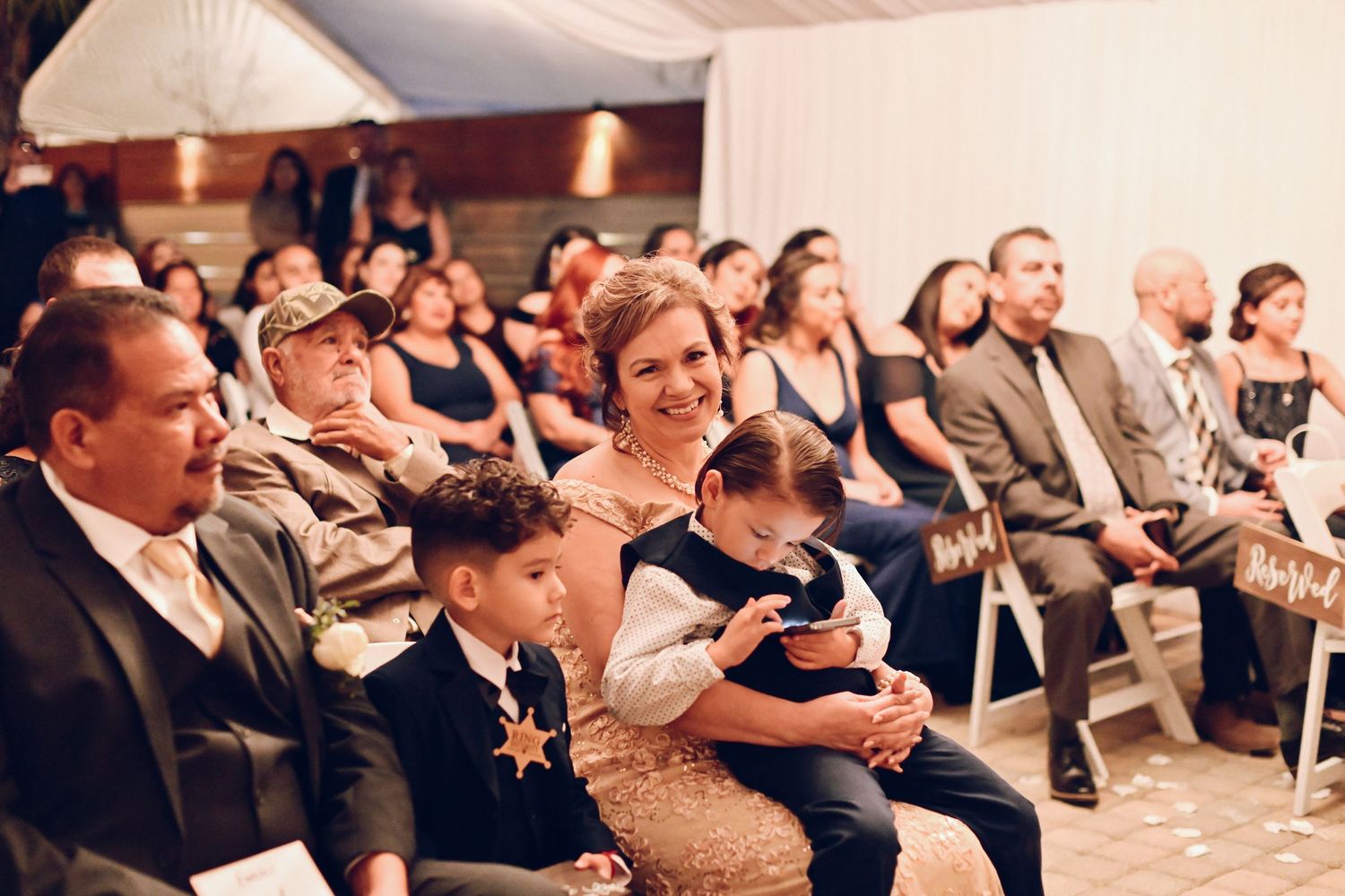 Wedding guests seated in rows watching ceremony proceedings indoors.