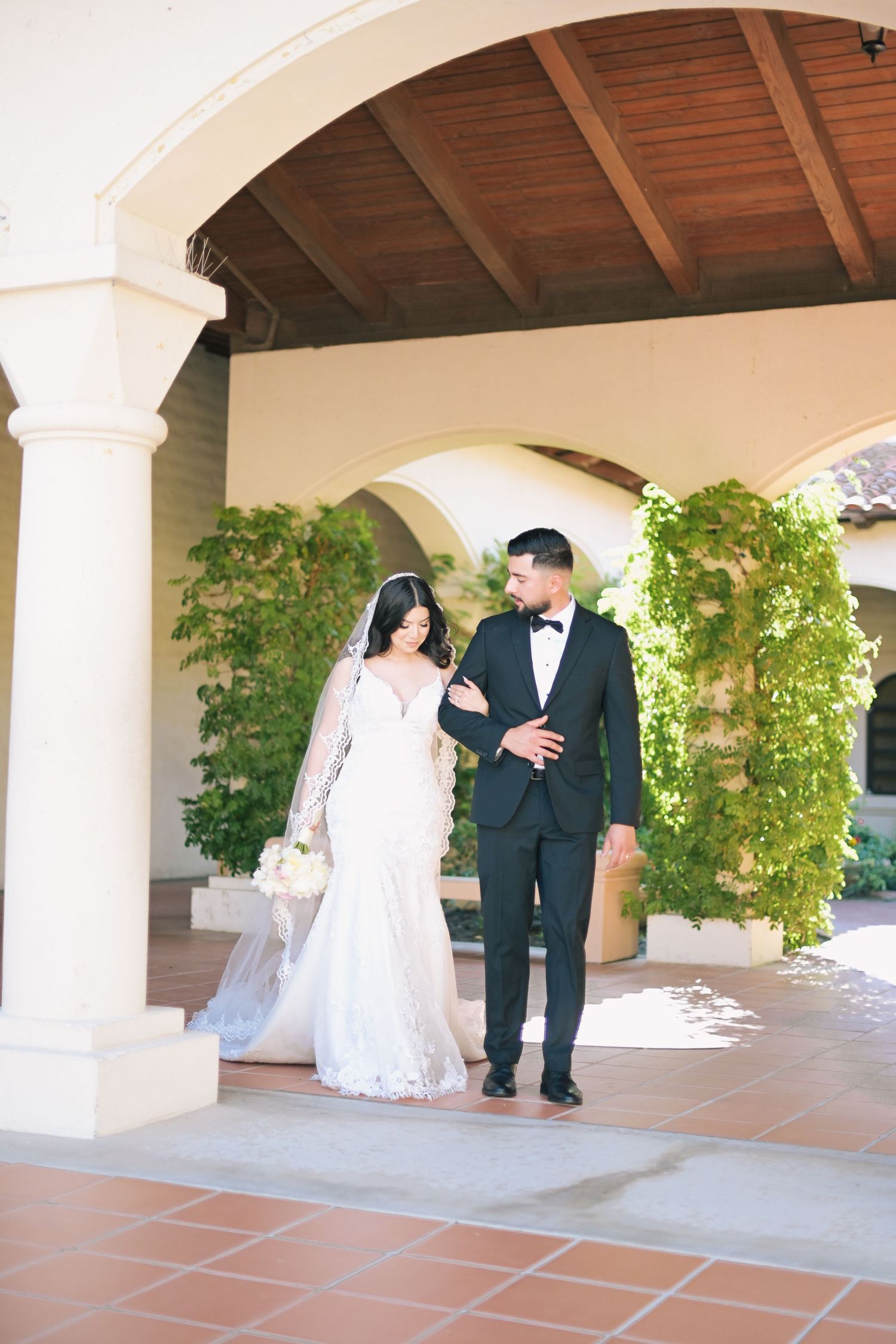 Elegant couple walking under Mediterranean-style arches with climbing greenery.