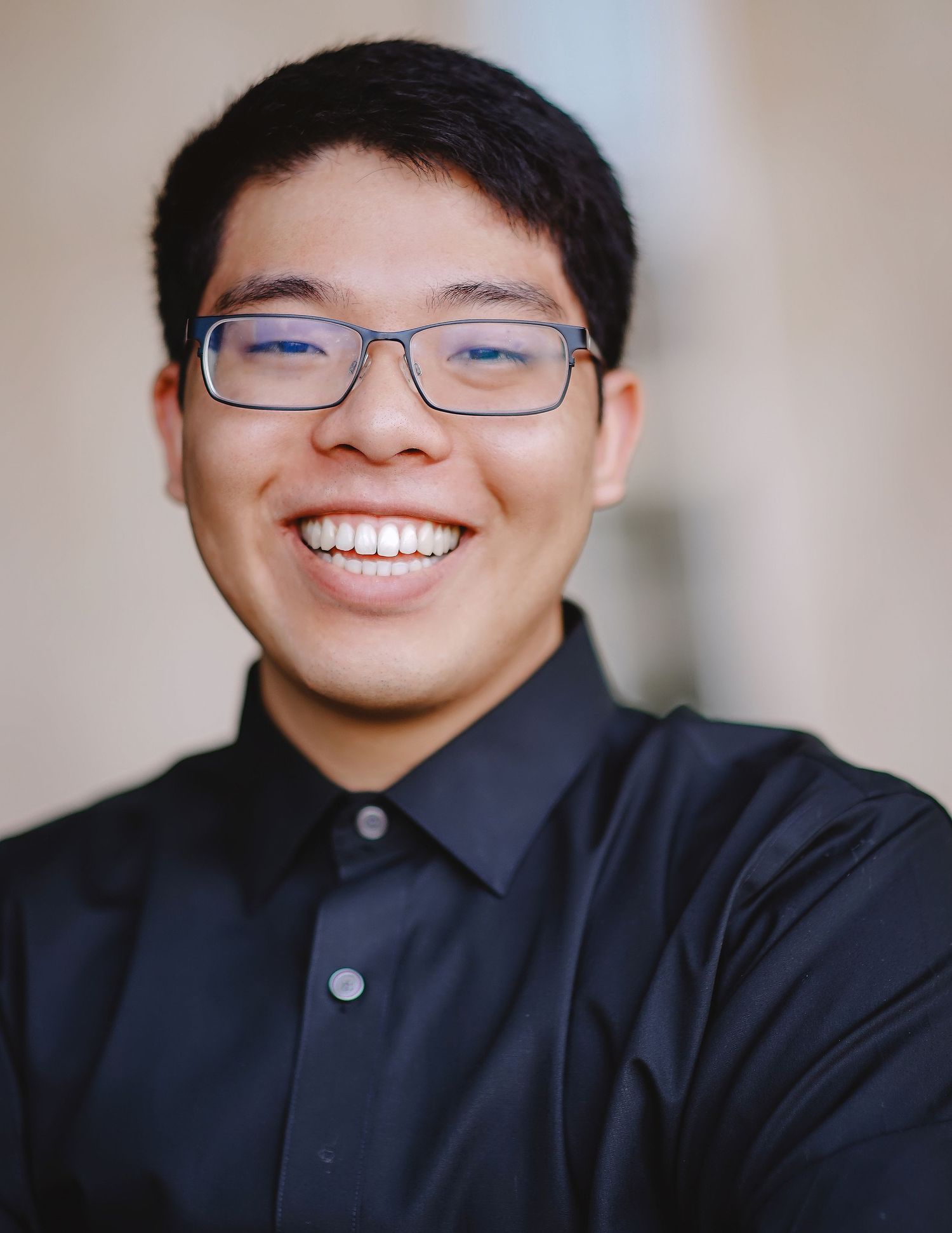 Professional headshot of person wearing glasses and dark polo shirt with bright genuine smile.