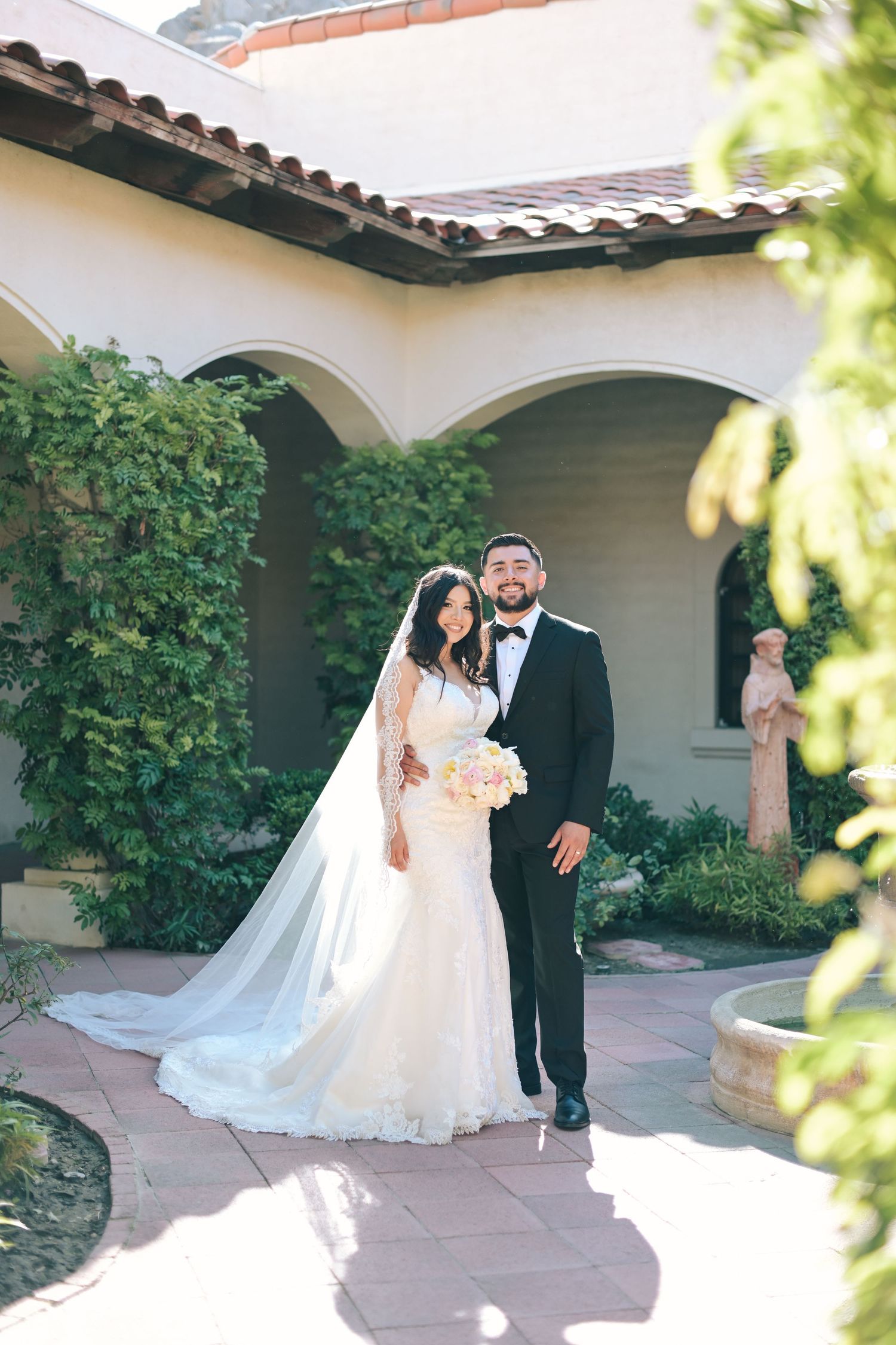 Wedding couple posing in front of Spanish-style building with arches and climbing vines.