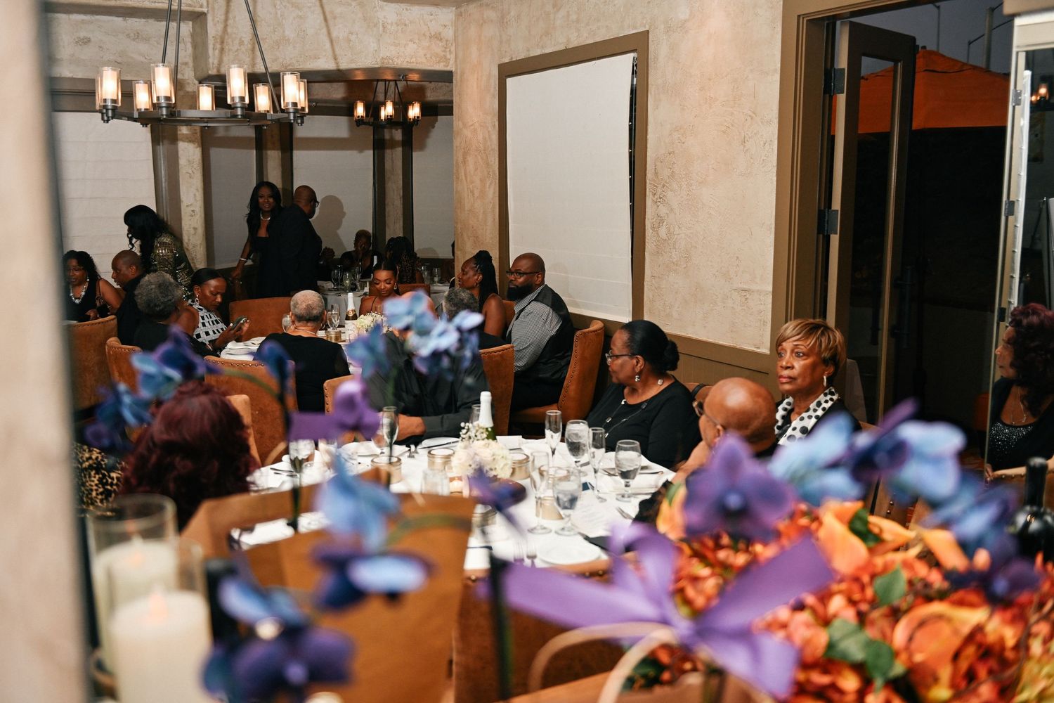 An indoor dining event with tables decorated with blue flowers and ambient lighting.