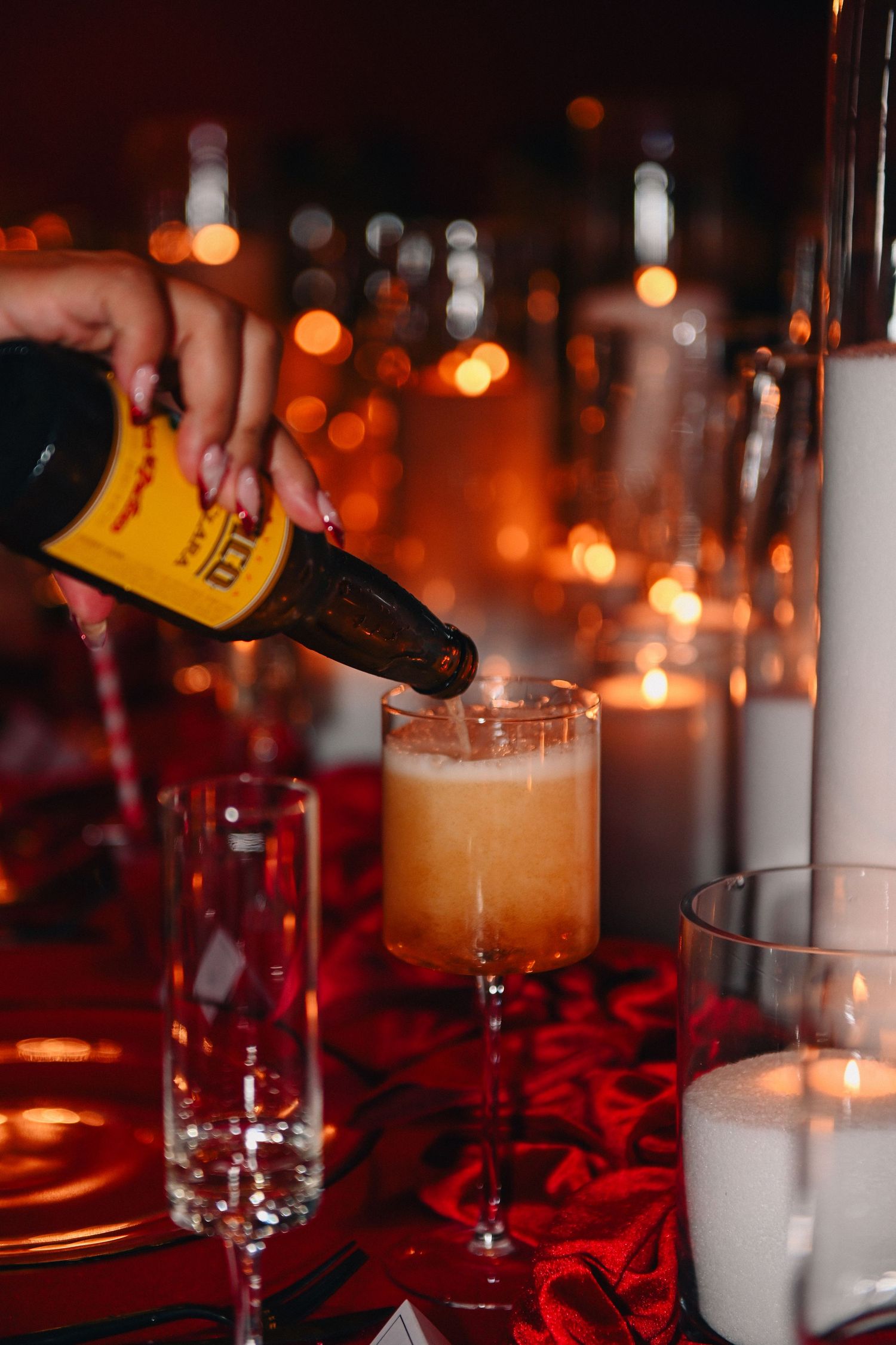 Hand pouring a craft cocktail into glass with bokeh lights in background.