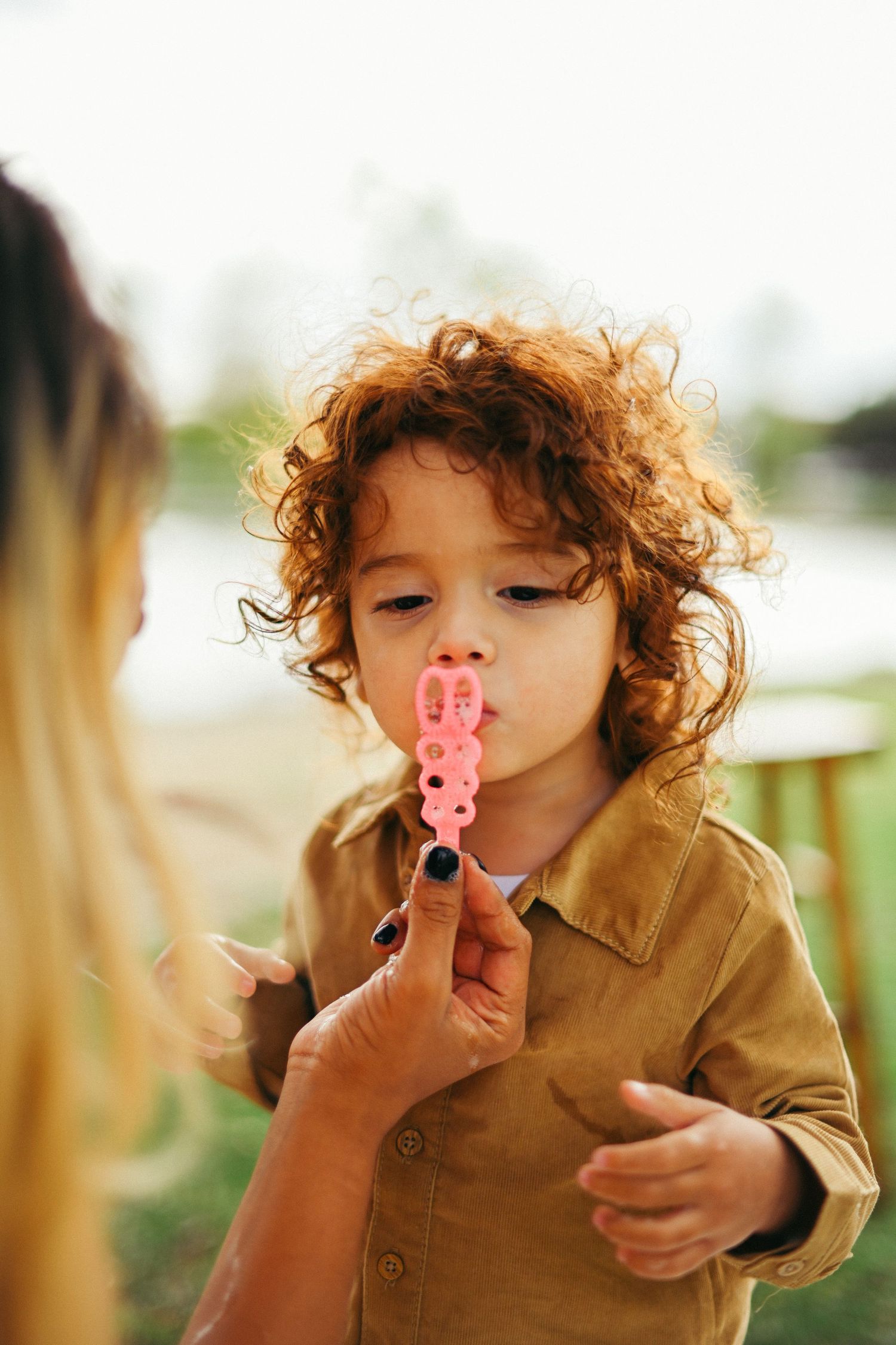 Child with curly hair blows bubbles while playing outdoors.