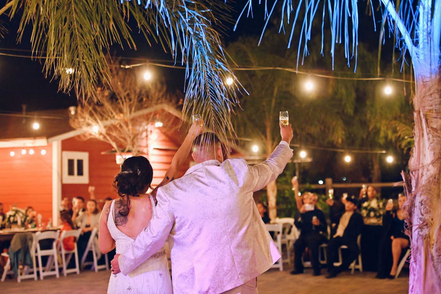 Couple dancing under palm trees at a nighttime wedding celebration with soft lighting.