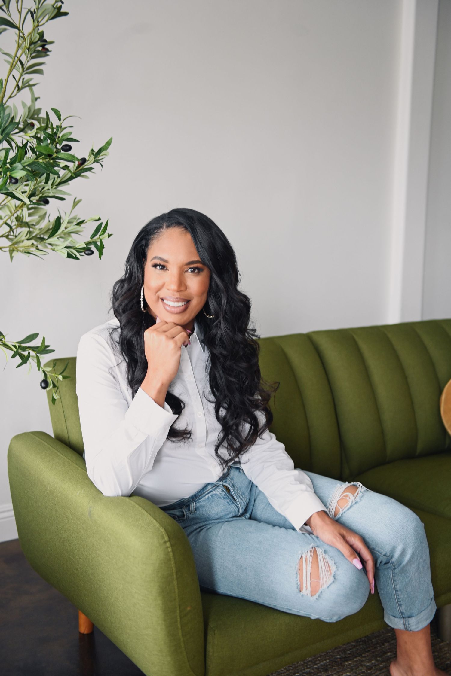 Woman in casual attire sitting on olive green couch in modern interior setting.
