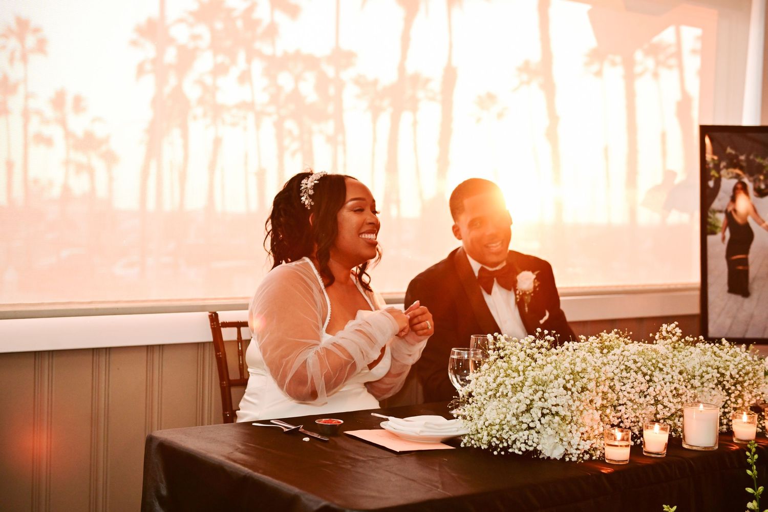 Warm sunset light illuminates a wedding reception table decorated with baby's breath and candles.