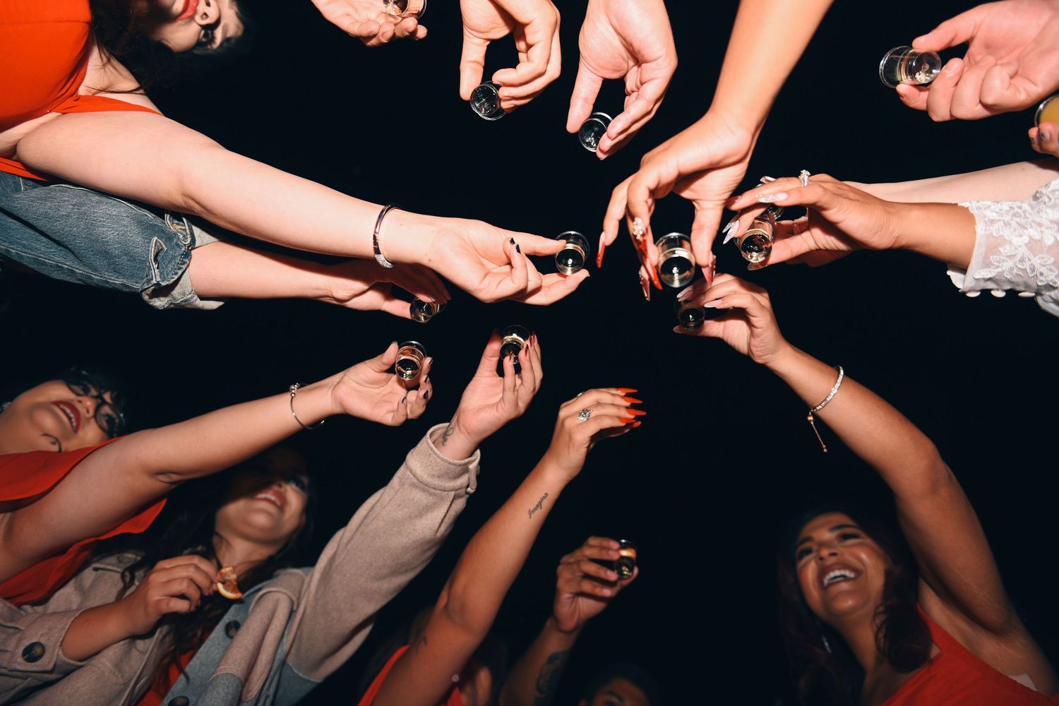 People reaching their hands toward the center in a circle while laughing and celebrating at a party.