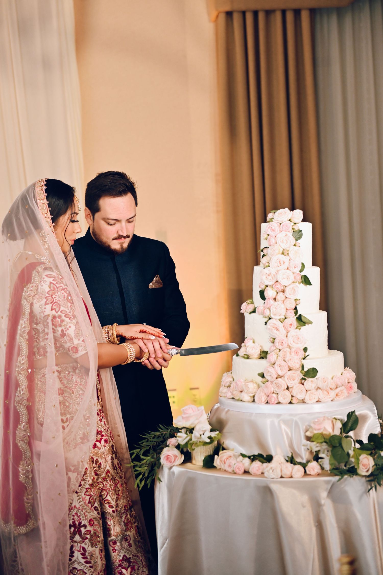 Wedding couple cutting an elegant five-tier white cake decorated with pink flowers.
