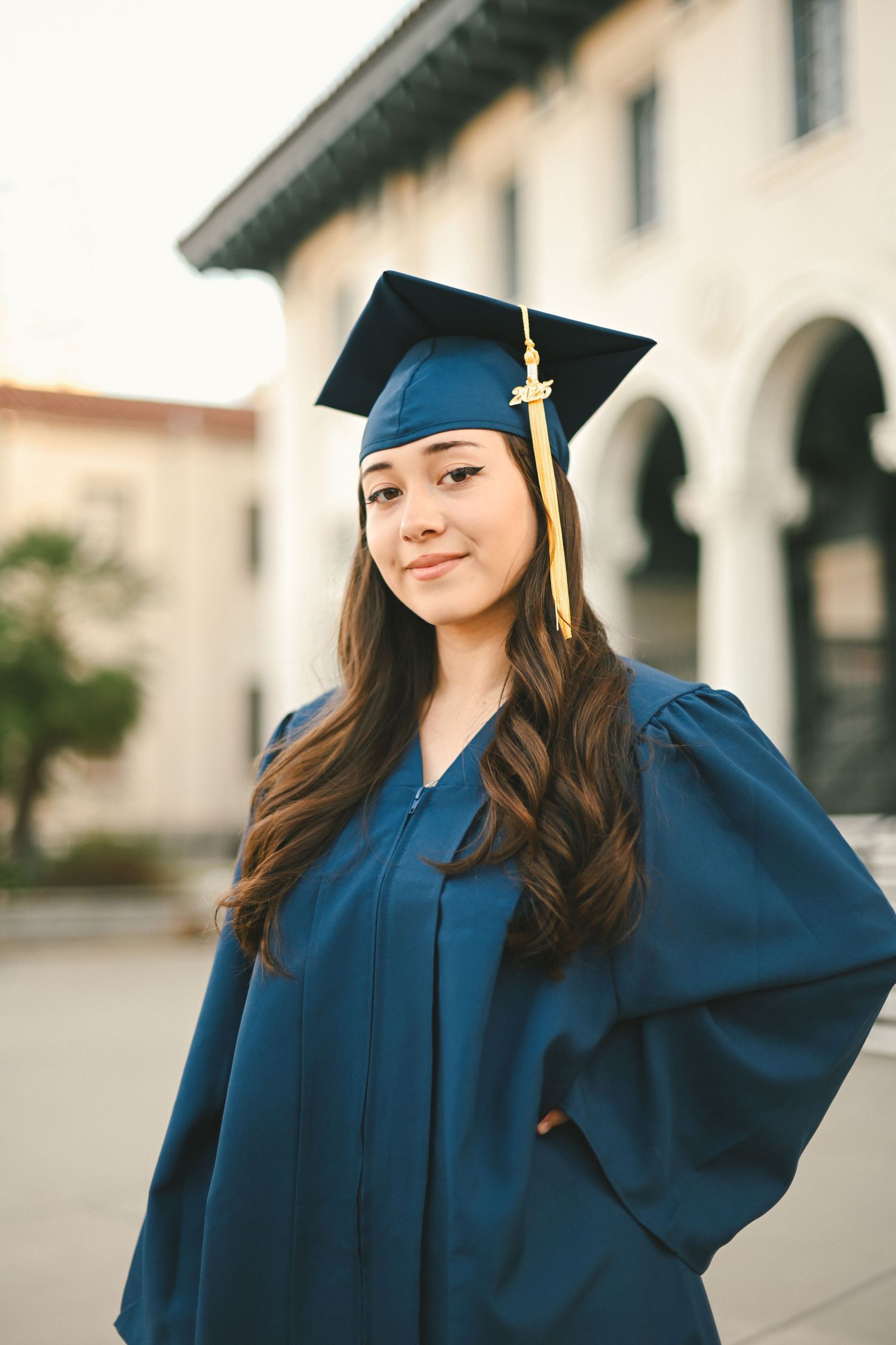 A graduation photo showing a student in a navy blue cap and gown with gold tassel against an architectural backdrop.