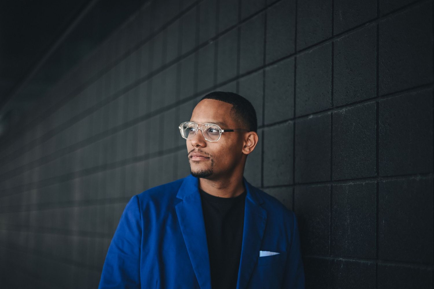 Professional portrait of person in blue blazer against dark geometric wall.