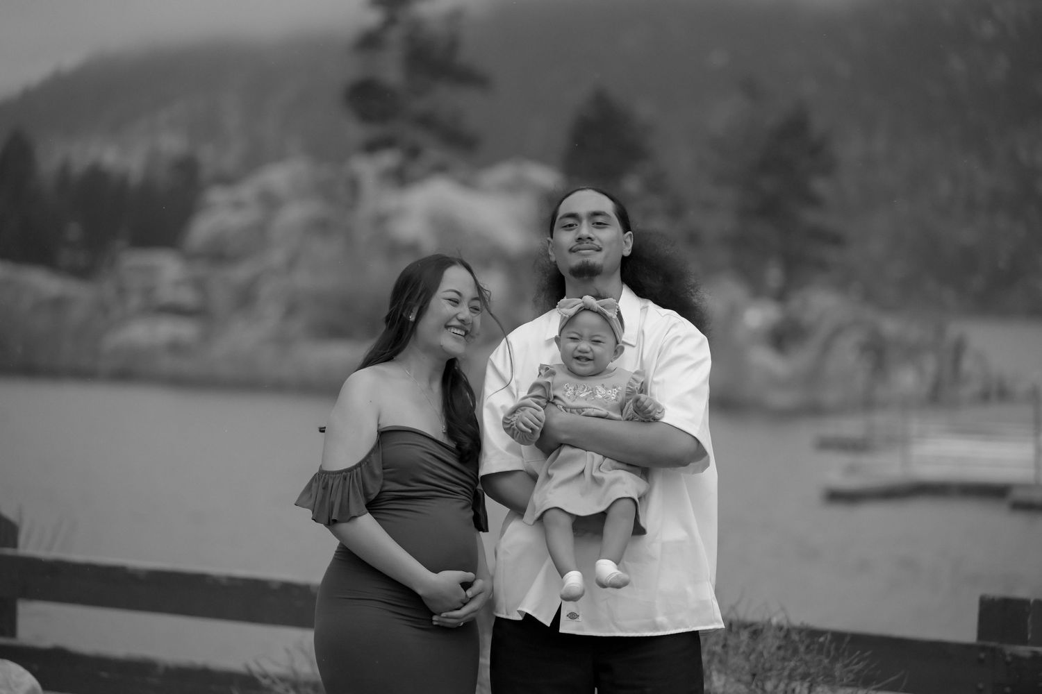 Black and white portrait of expecting couple with baby surrounded by mountain landscape.