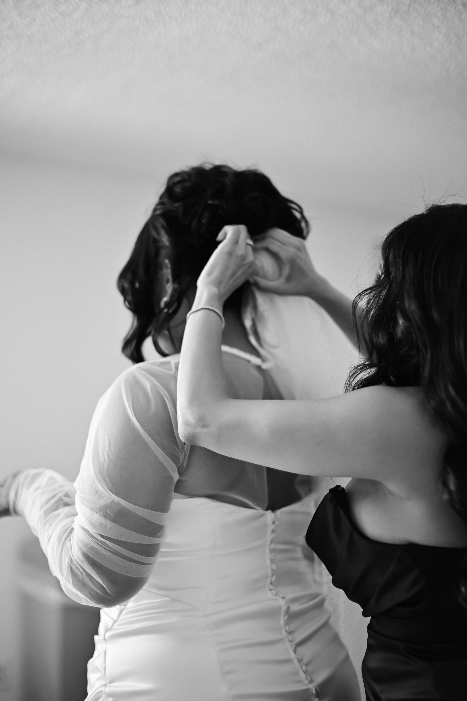 Someone helping adjust a wedding dress in an intimate black and white moment.