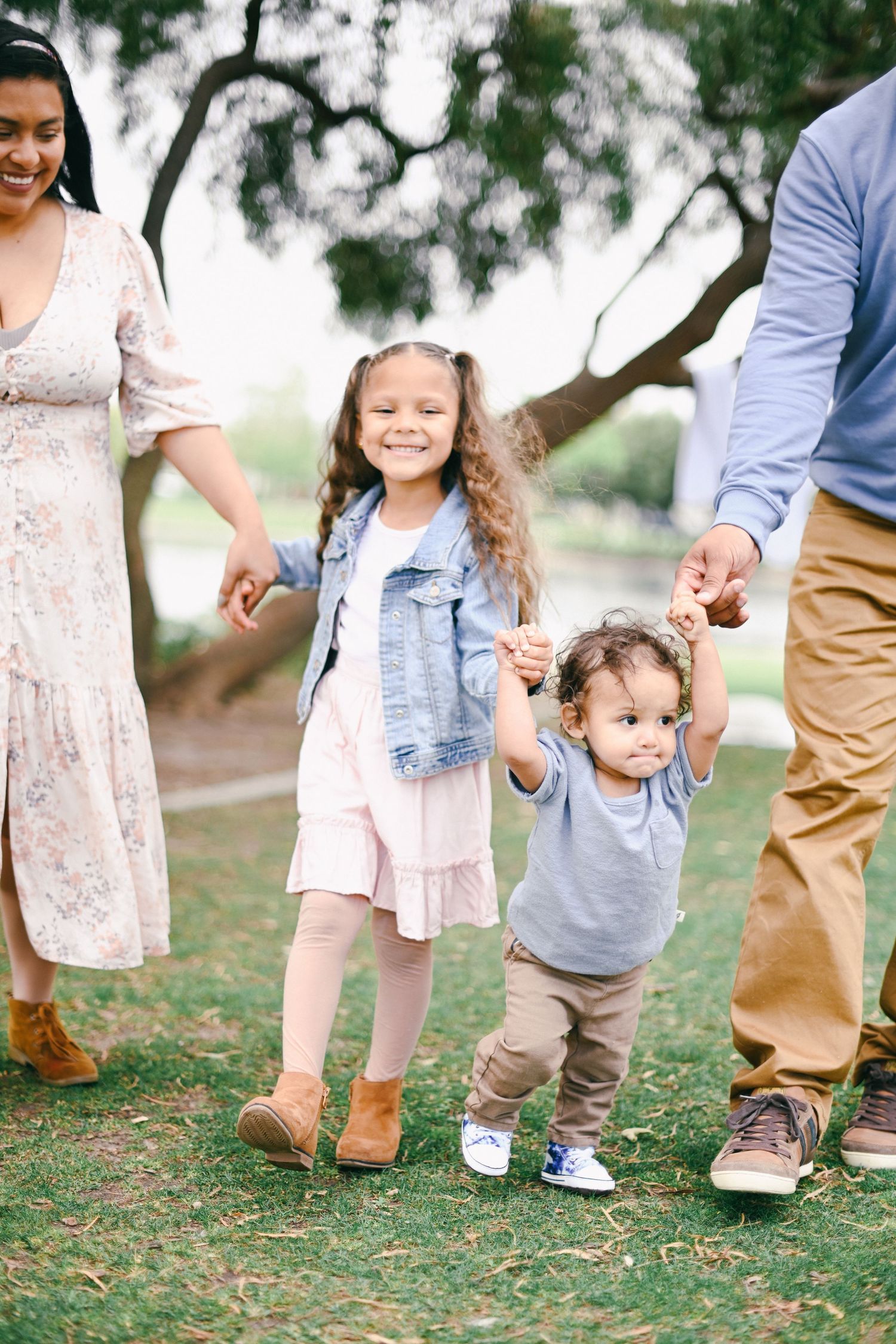 Family walking together outdoors on grass near trees holding hands.